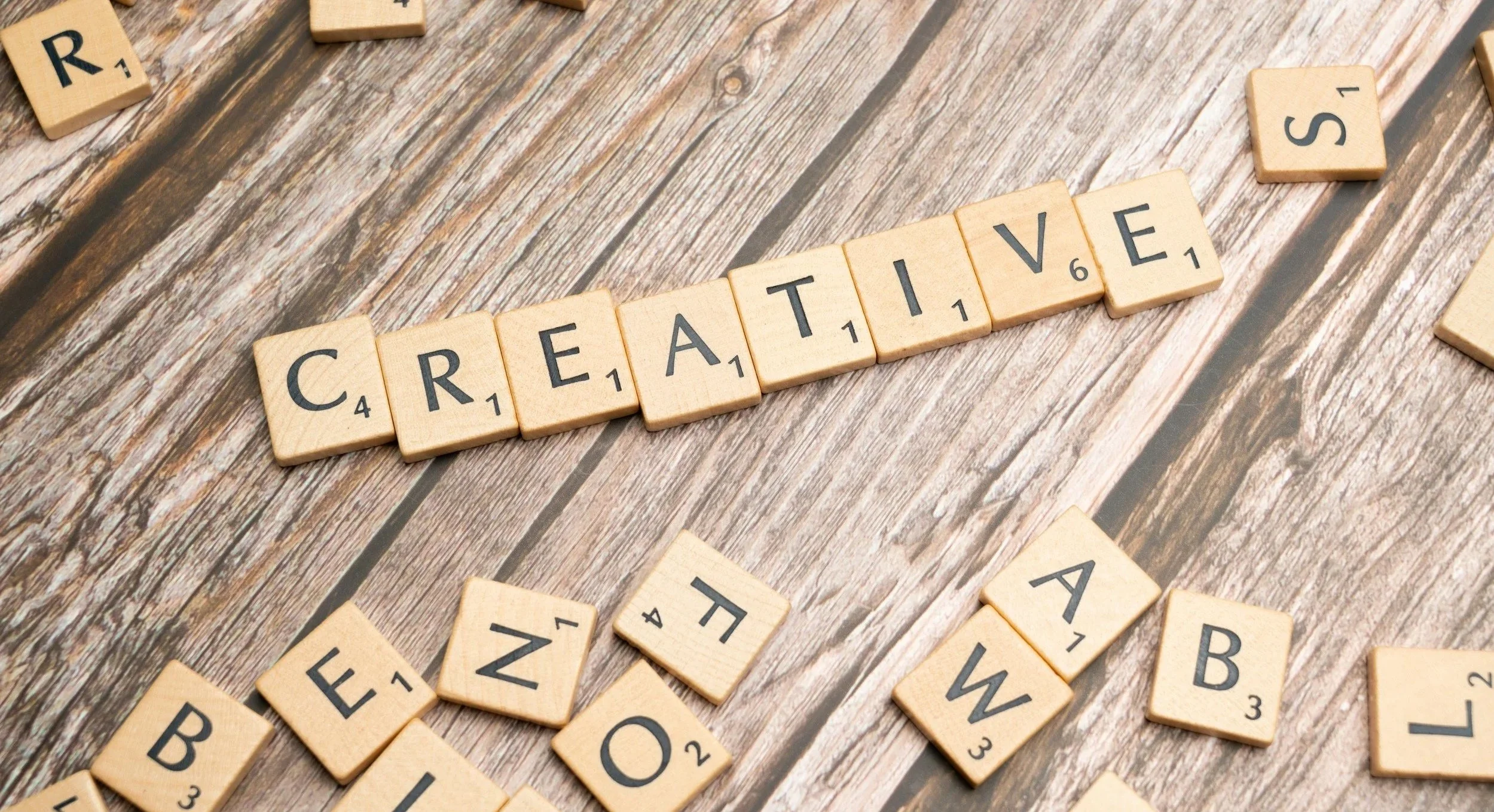 Scrabble tiles spelling out 'CREATIVE' on a wooden surface.