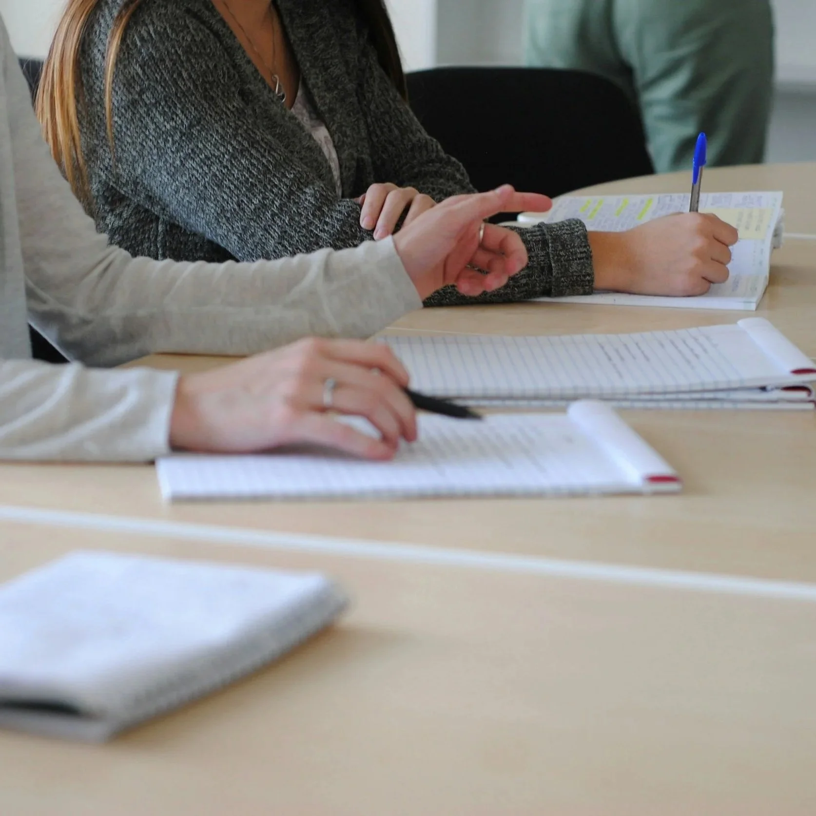 Pessoas participando de uma reunião ou aula, escrevendo em cadernos com post-its, em uma sala de conferência.