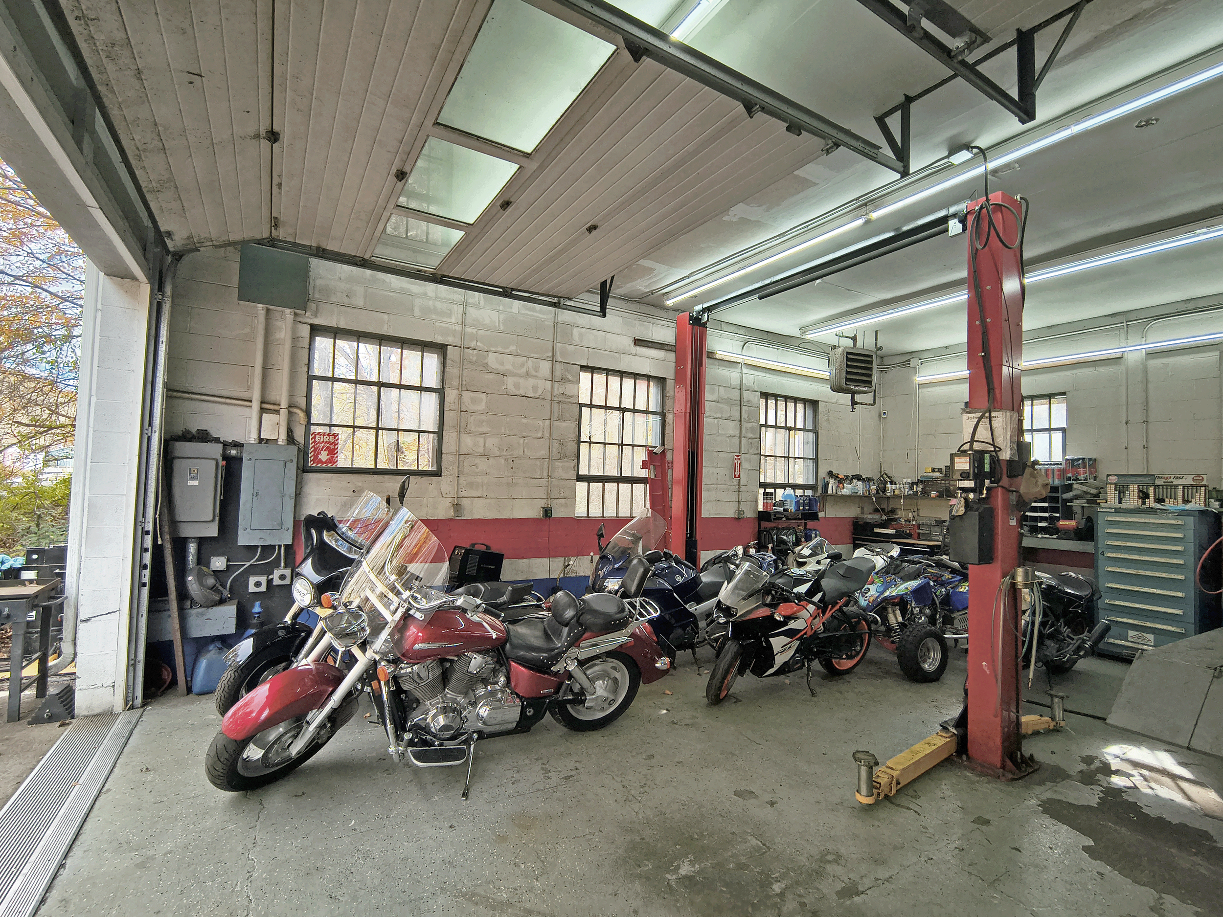 Interior view of a motorcycle repair garage with multiple motorcycles, tools, and equipment.