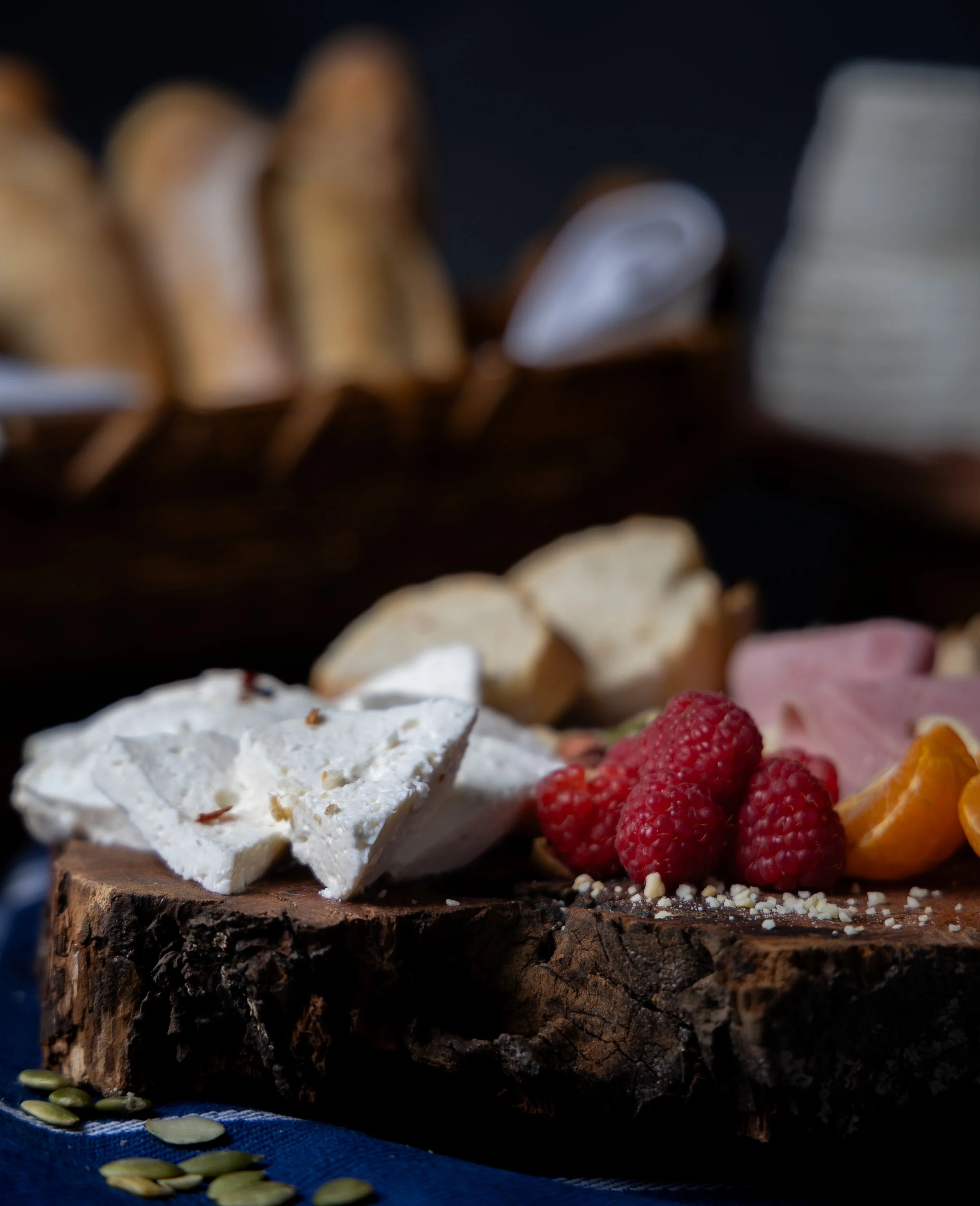 Cheese, raspberries, ham, and orange slices on a wooden serving board.