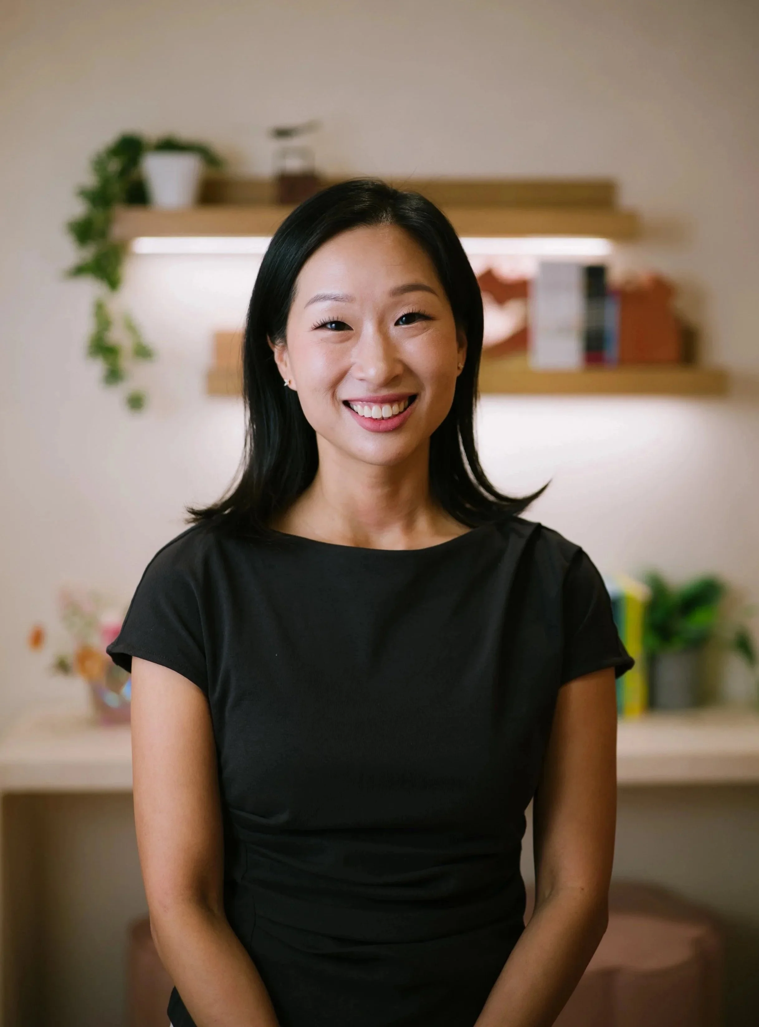 Smiling woman with shoulder-length black hair, wearing black scrubs and necklace, standing.