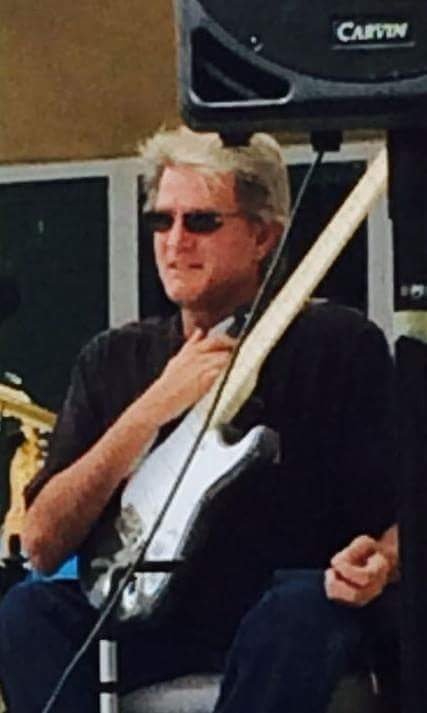 A man with gray hair wearing sunglasses, sitting outdoors, holding a guitar, with audio equipment nearby. Stephen Twist, Nashville Bound, Lonely Just Goes On, Broken Heart Surgery, Stormy Night, Little Darli', Maybe Not, COVID 19 Blues, Tony Stoufer