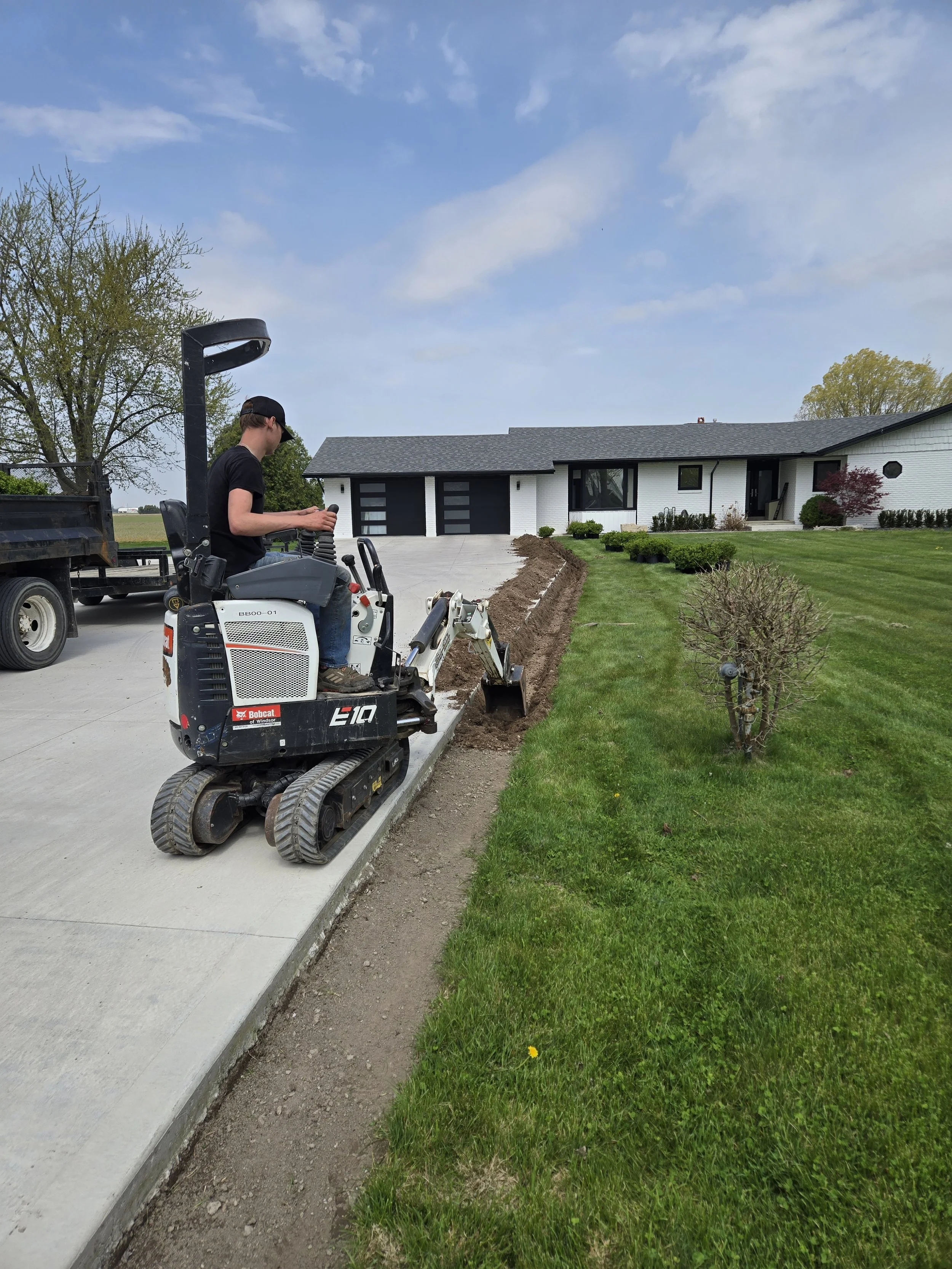Man on tiny excavator grading the side of the driveway