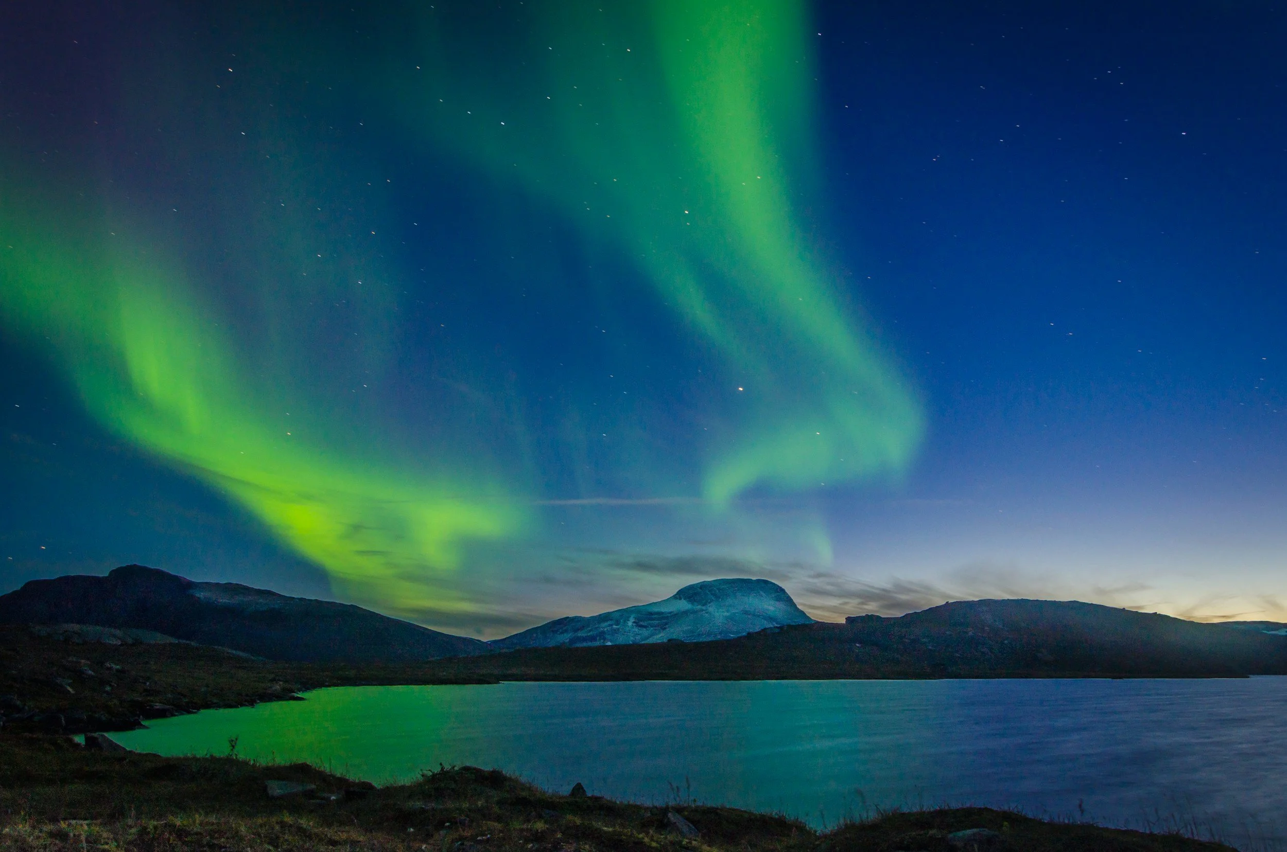 Northern lights over mountains and a lake at night with a starry sky.