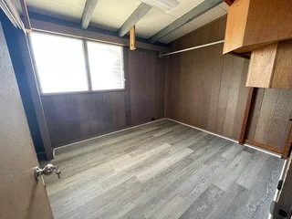 Empty room with wood-paneled walls, large window, and light gray flooring.