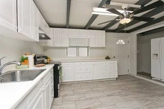 Empty modern kitchen with white cabinets, gray tiled floor, and a ceiling fan.