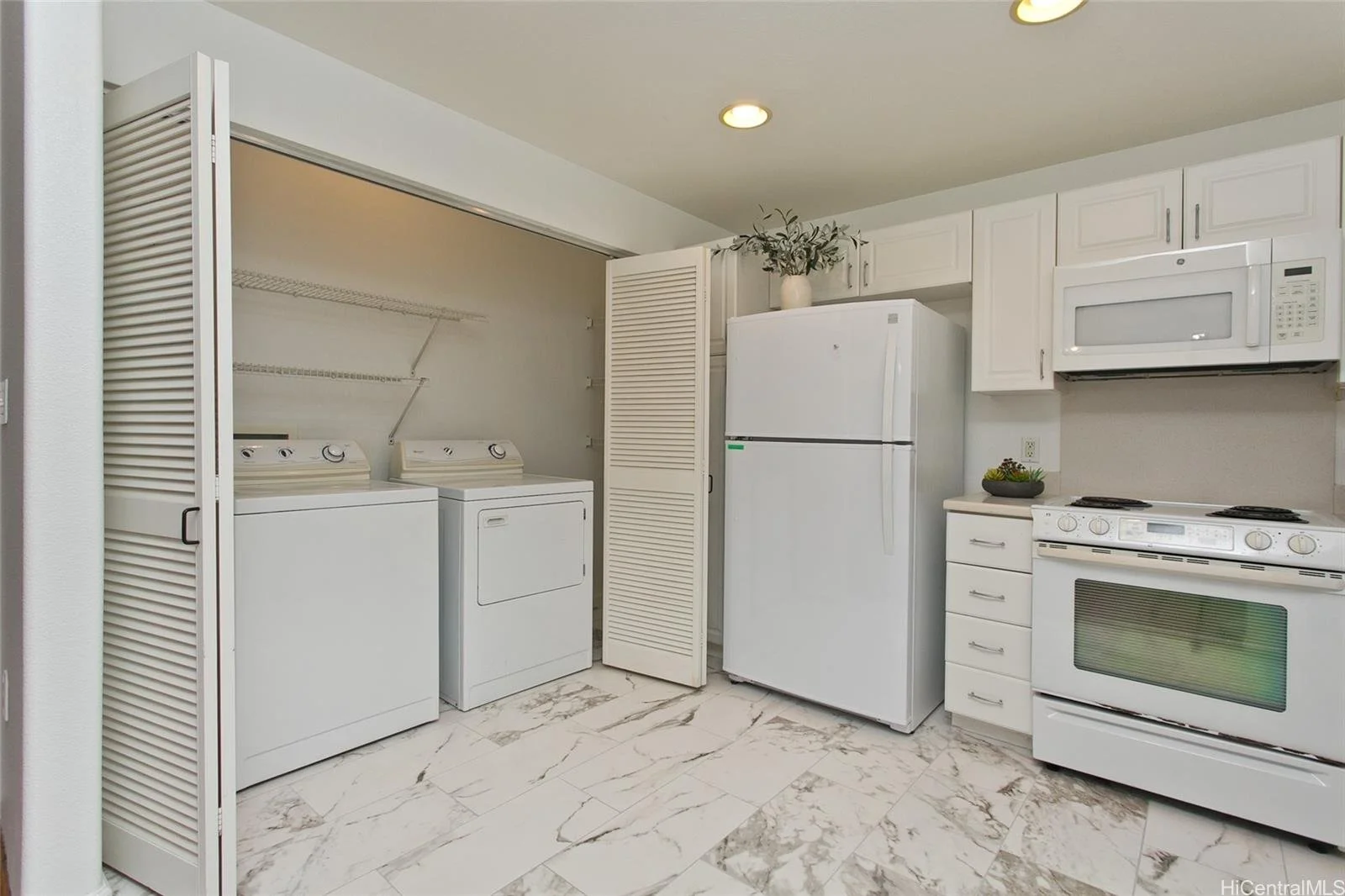 Laundry area with washer and dryer inside a closet space, kitchen appliances such as refrigerator, microwave, and stove, with white cabinetry and marble flooring.