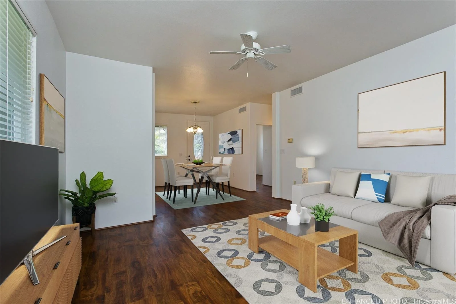 Living room with white sofa, wooden coffee table, gray and beige patterned rug, and wall art; dining area with table and chairs in the background.