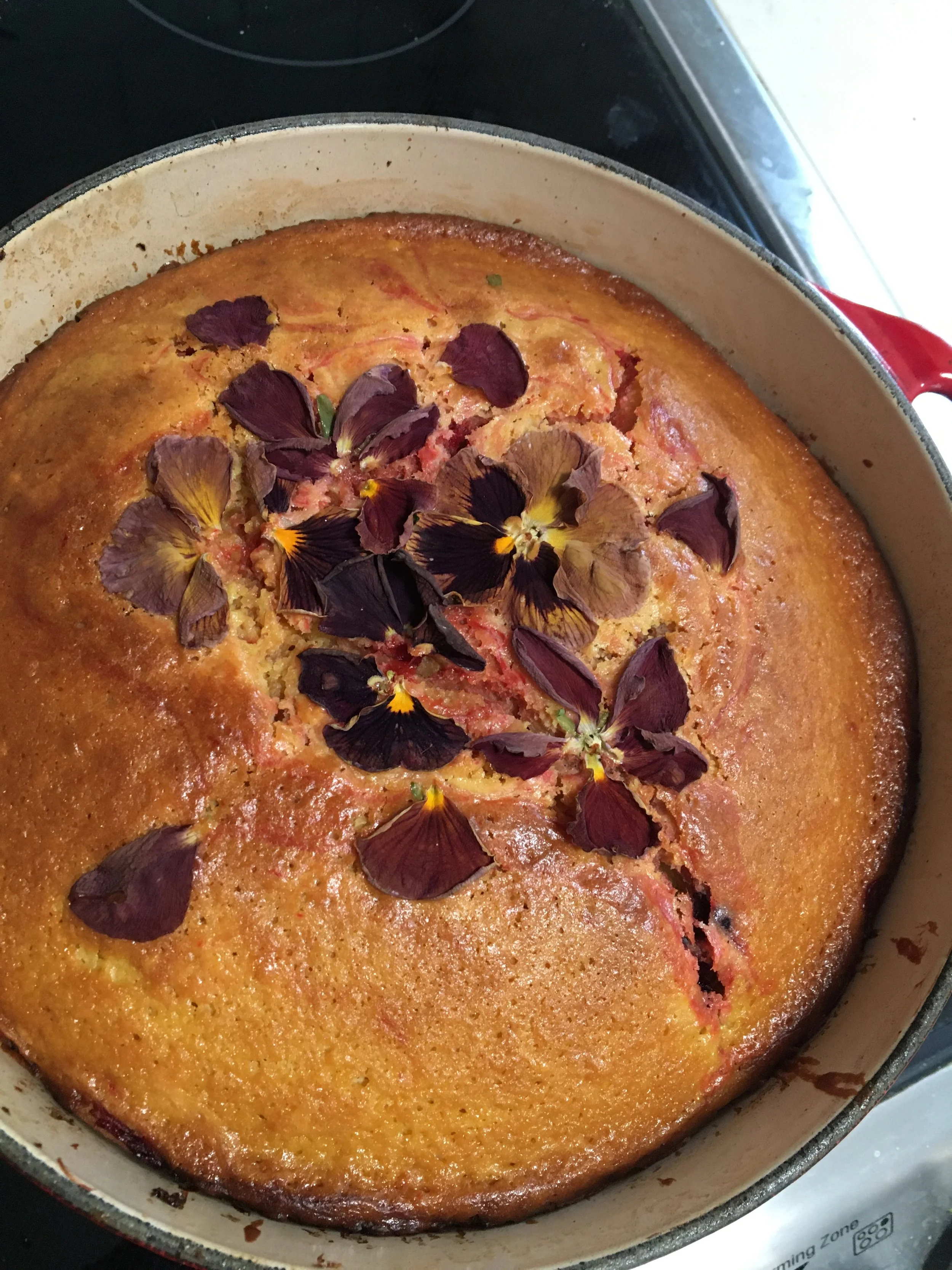 Golden baked cake topped with purple edible flowers in a round baking dish