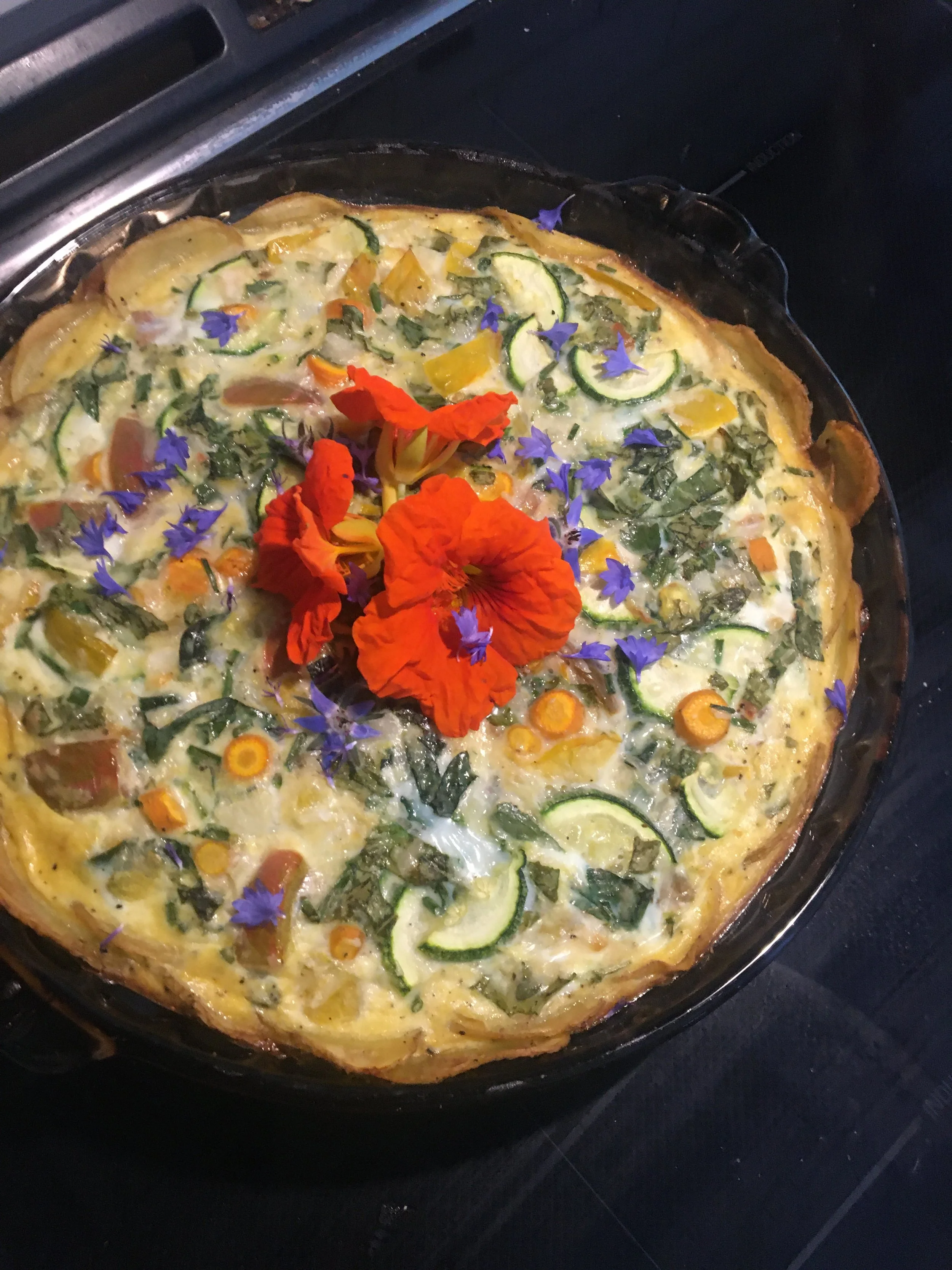 Vegetable frittata garnished with edible flowers, including orange, purple, and yellow flowers.