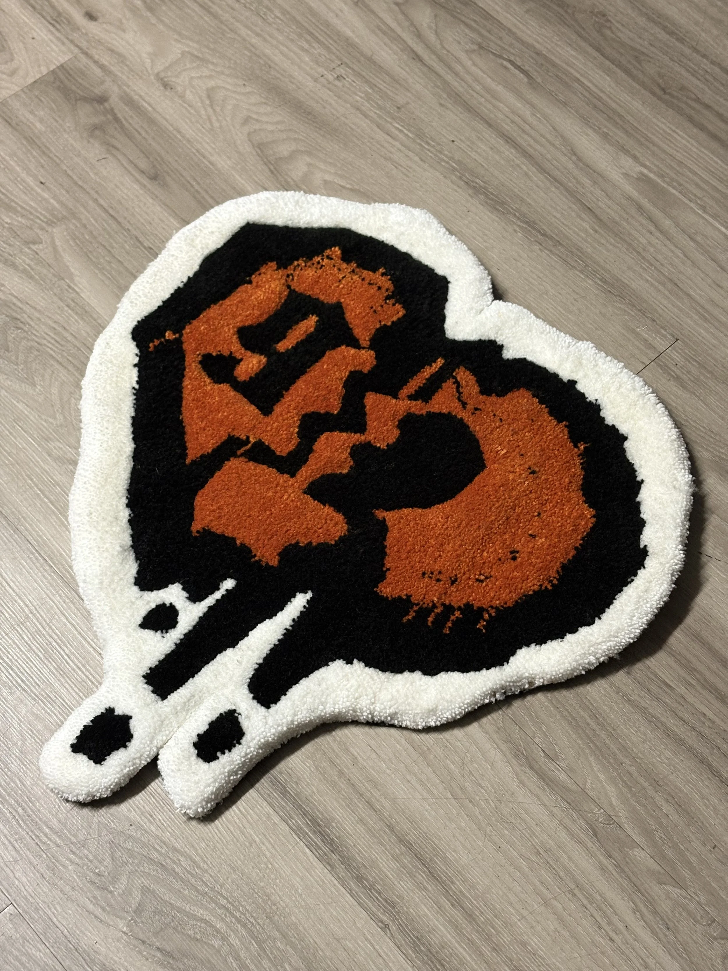 A bath mat shaped like a wine glass with an orange and black pumpkin face design.