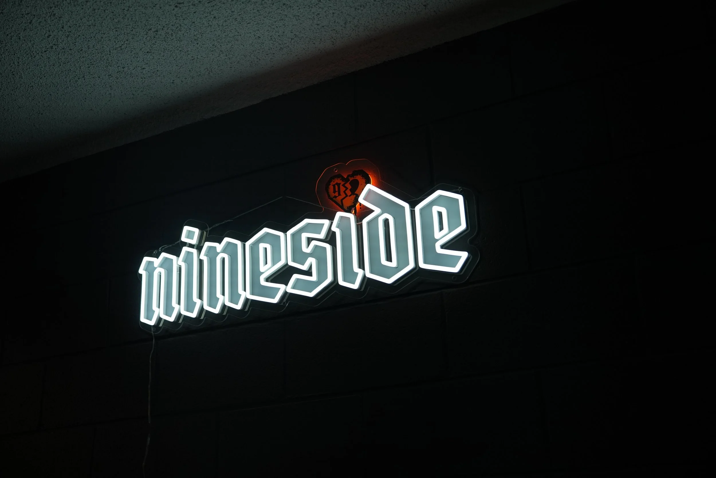 Neon sign in white letters spelling 'nineside' on a dark wall with a glowing red heart above the sign.