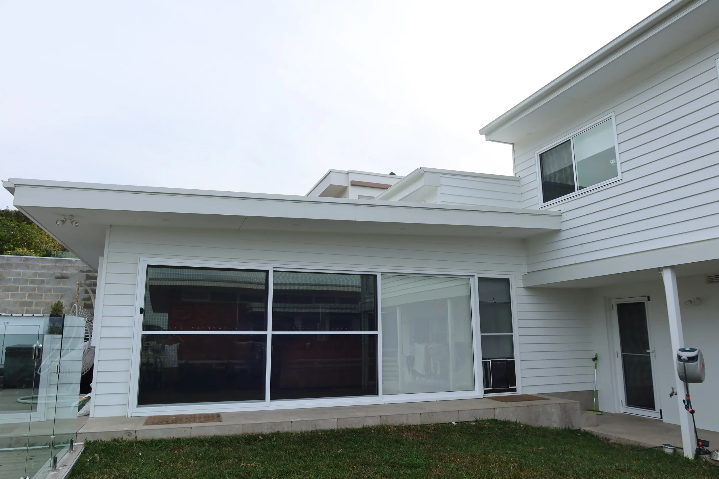 Rear exterior view of a modern white house with sliding glass doors, a small concrete patio, and tall grass in the yard.