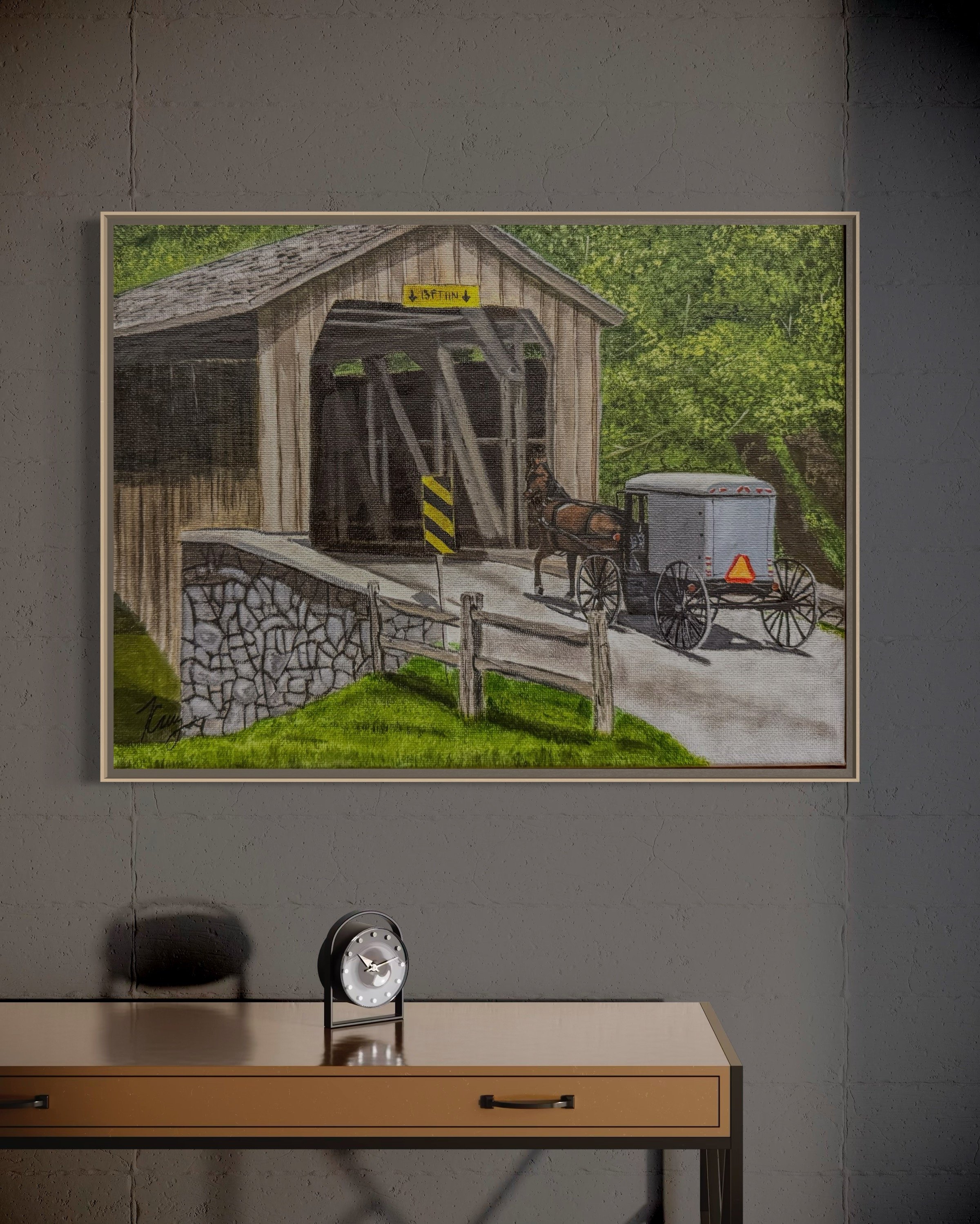 Painting of a covered bridge with a horse-drawn wagon outside, set against trees and grass, hanging on a gray wall.