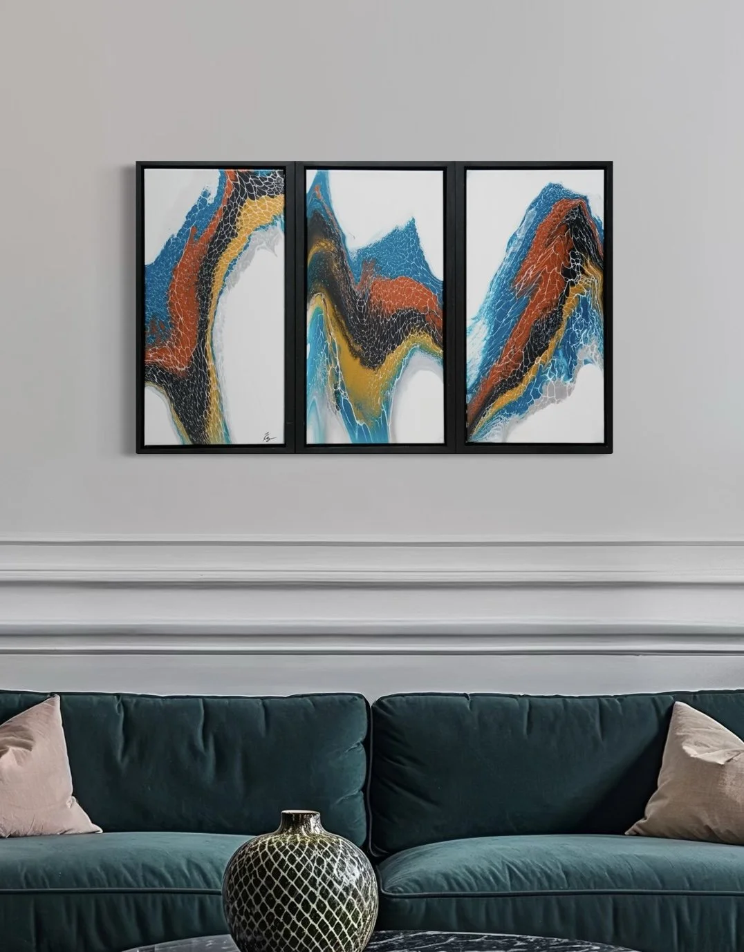 A triptych abstract painting with vibrant swirling patterns in shades of blue, orange, black, yellow, and white, hanging on a white wall above a dark green velvet sofa with beige pillows.