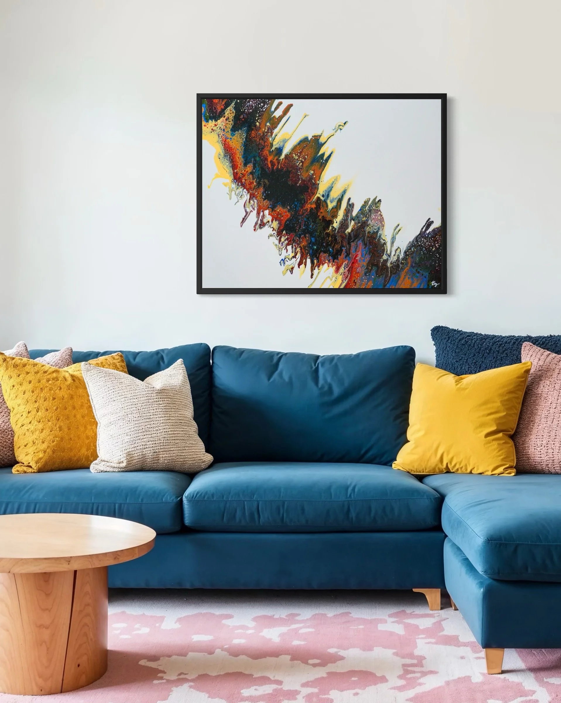 Living room with a blue sectional sofa, colorful throw pillows, a round wooden coffee table, a pink and white rug, and an abstract painting with vibrant colors on the wall.