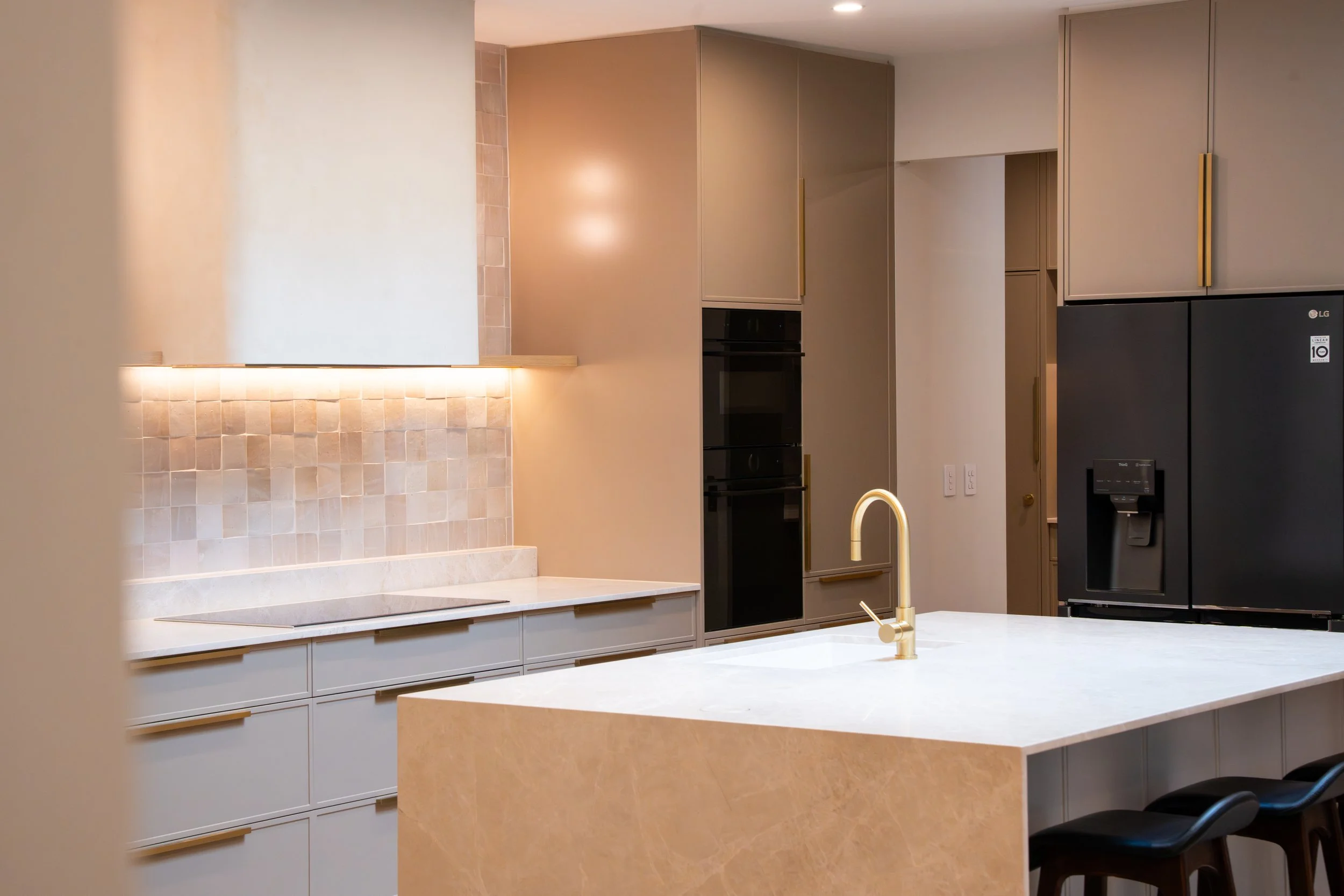 Modern kitchen with beige cabinetry, black refrigerator, and a marble kitchen island with a gold faucet.