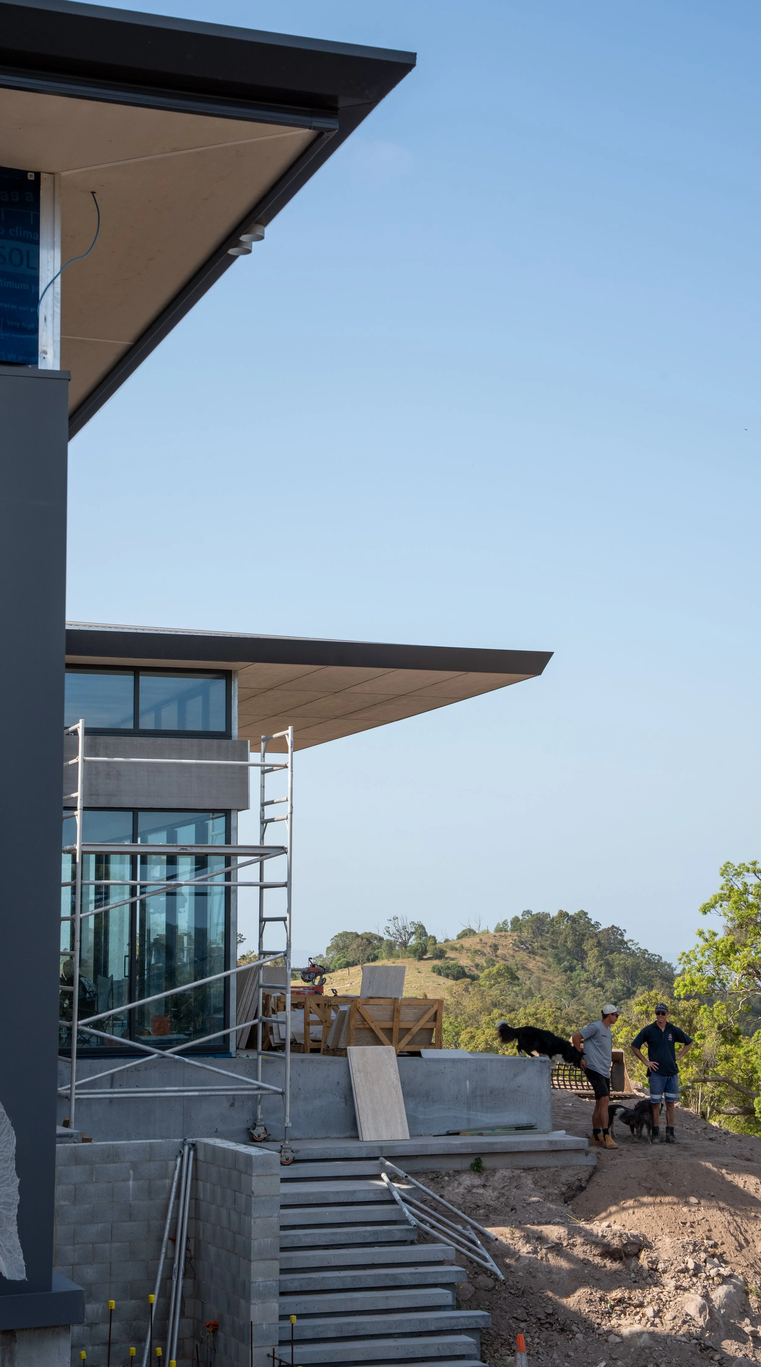 People with dogs on a construction site of a modern house with hills in the background.