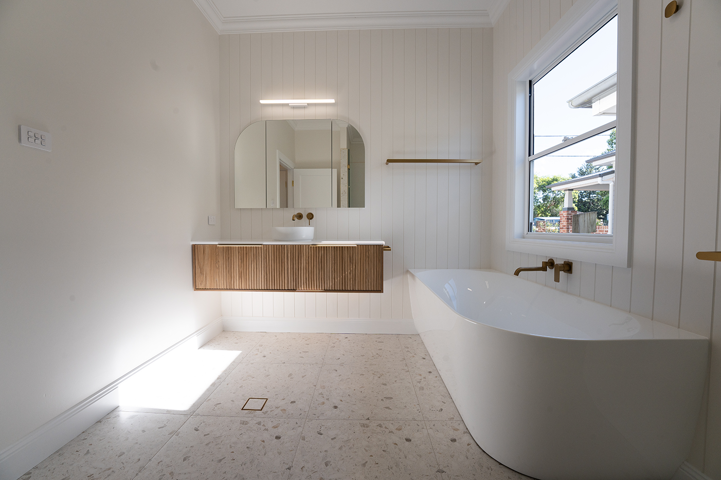 Modern bathroom with a freestanding bathtub, vanity with a vessel sink, large mirror, window, and minimal decor.