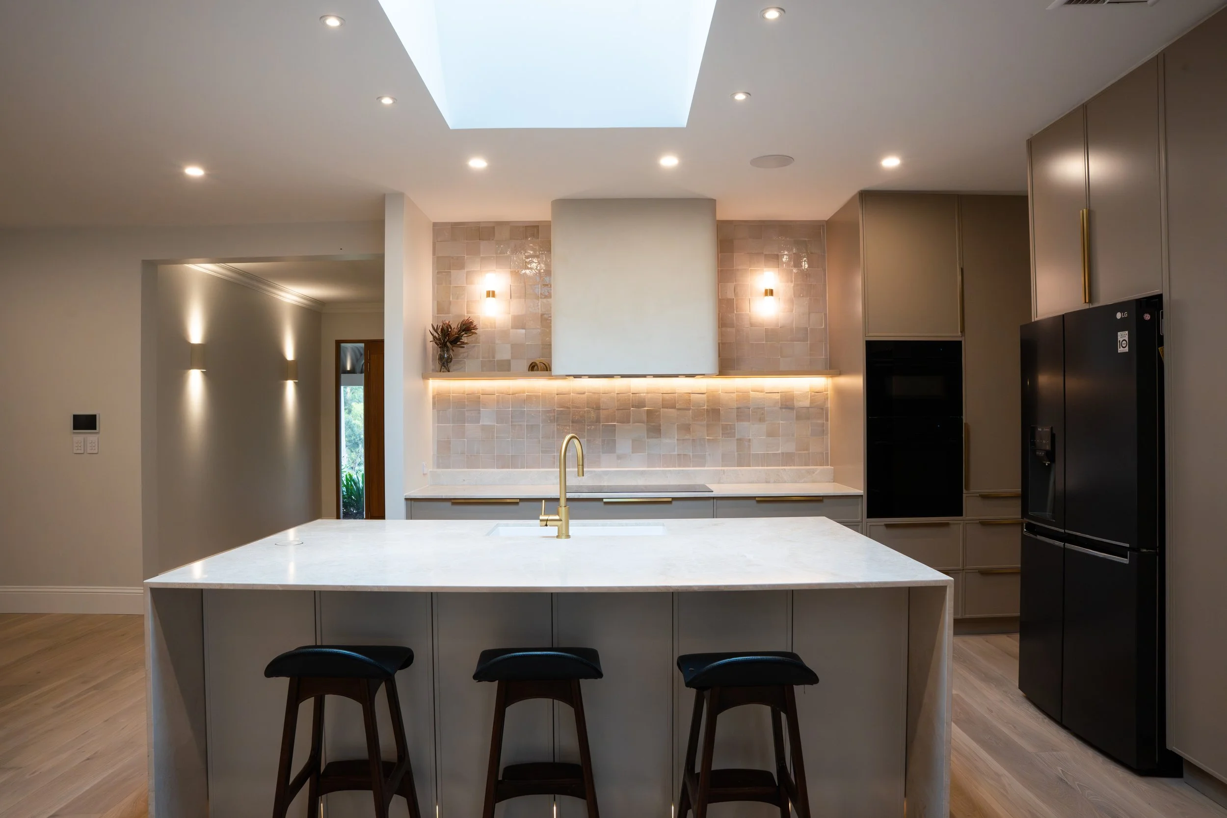 Modern kitchen with an island, black refrigerator, beige cabinets, and a skylight.