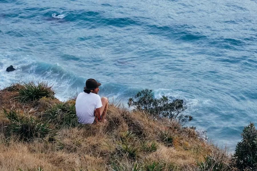 Person sitting on a grassy cliff overlooking the ocean