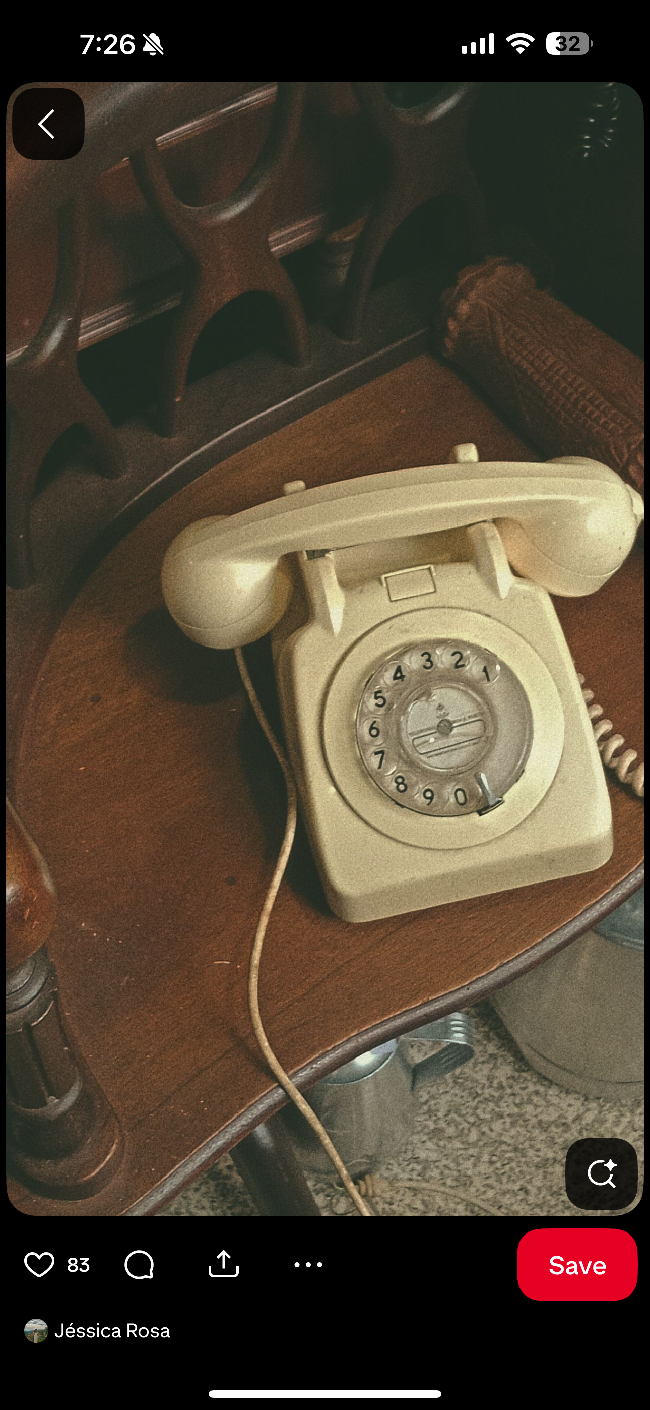 An old beige rotary dial telephone on a wooden table with a dark brown hand towel and part of a wooden chair visible.