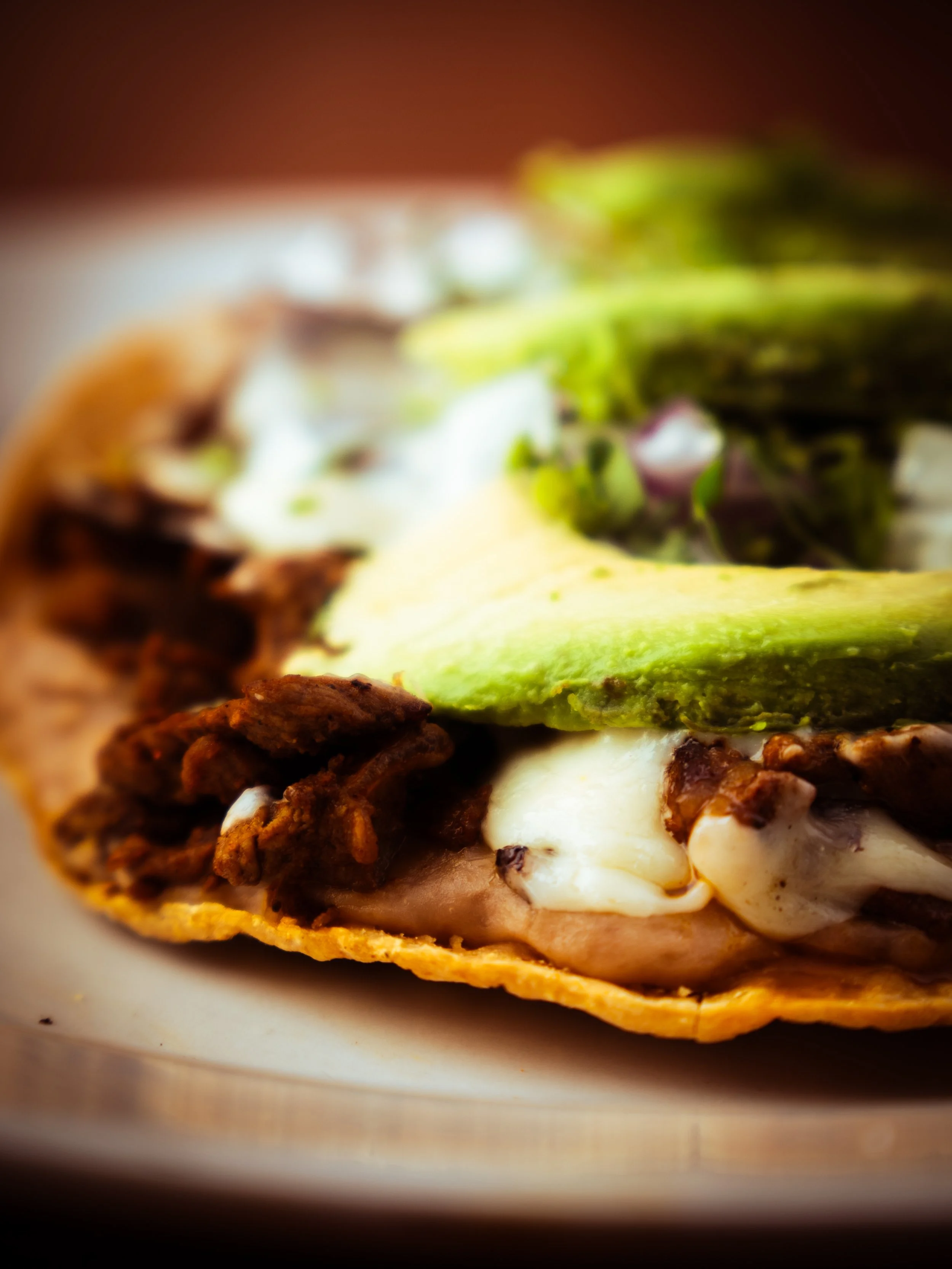 Close-up of a Volcanes with seasoned meat, cheese, lettuce, and avocado on a plate.