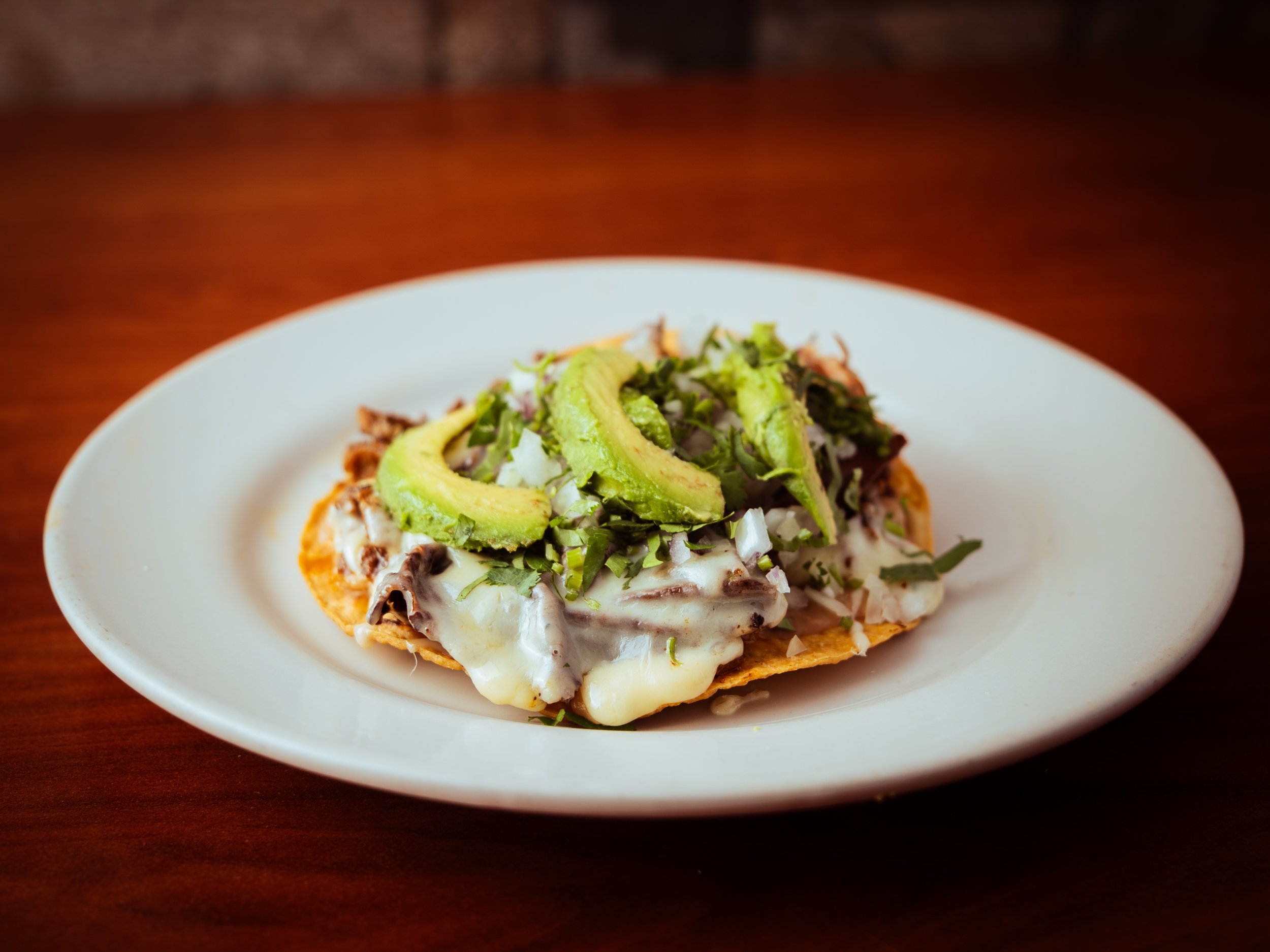 Close-up of an avocado and shredded beef Volcanes on a white plate placed on a wooden table