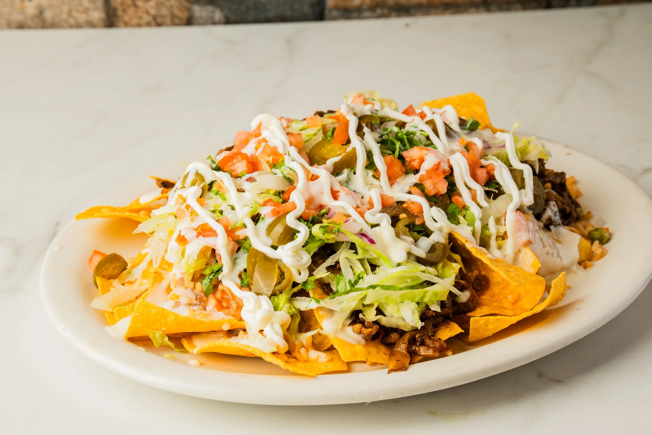 Plate of nachos with melted cheese, shredded lettuce, sour cream, chopped tomatoes, jalapeños, ground beef, and shredded cheese.
