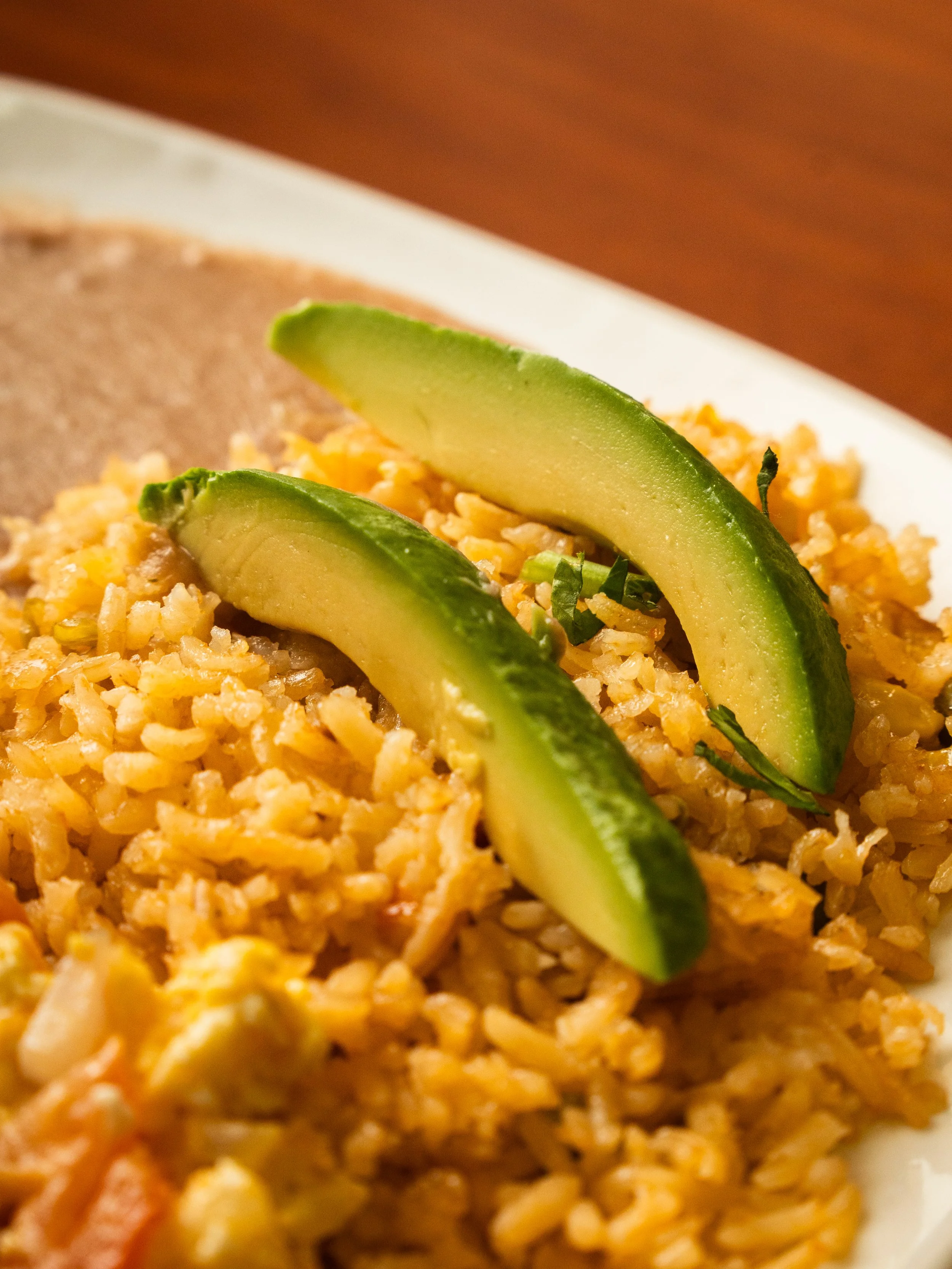 Close-up of a plate of scrambled eggs with sliced avocado on top.