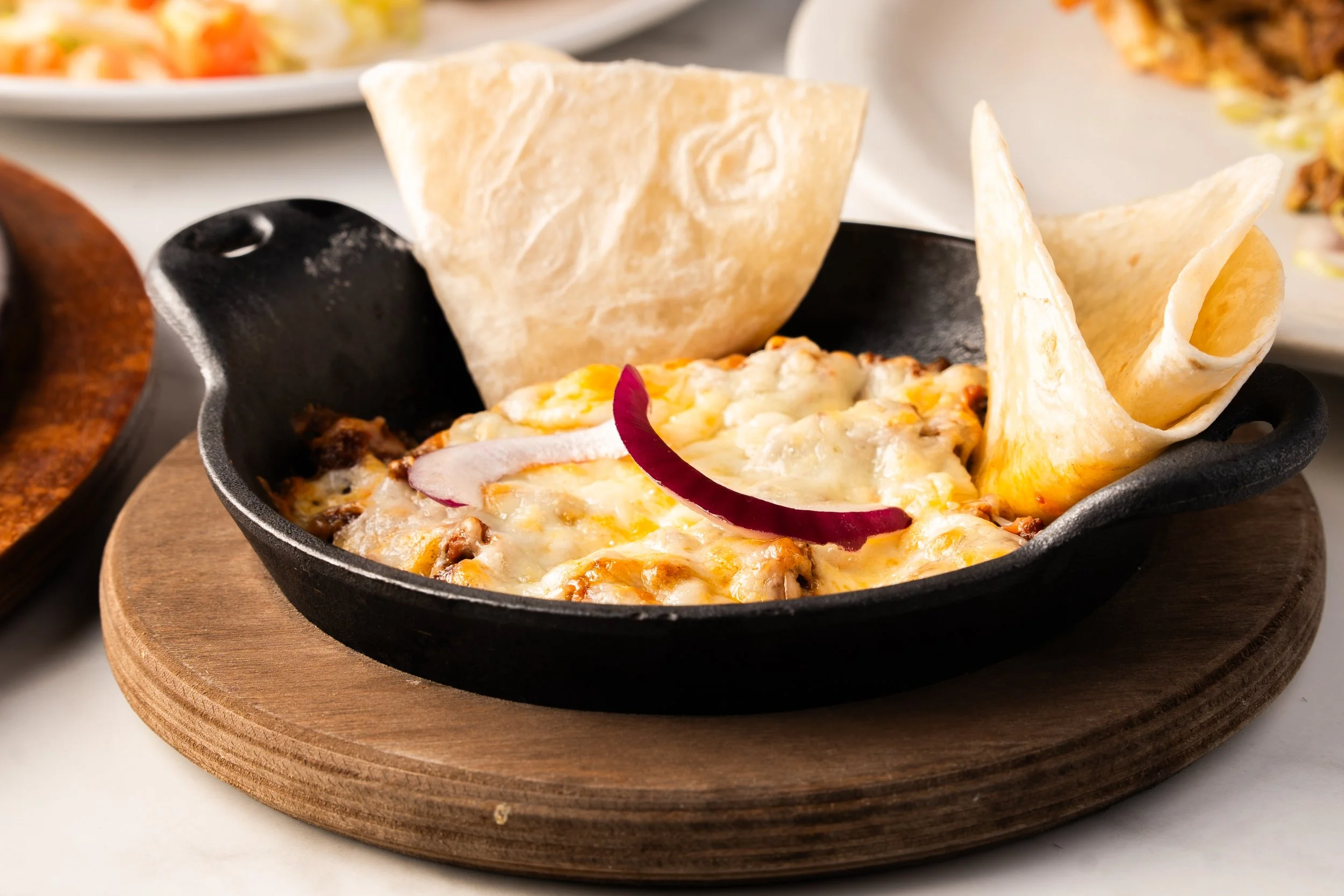 Chori-queso with tortilla chips and onion slices in a black skillet on a wooden serving board.