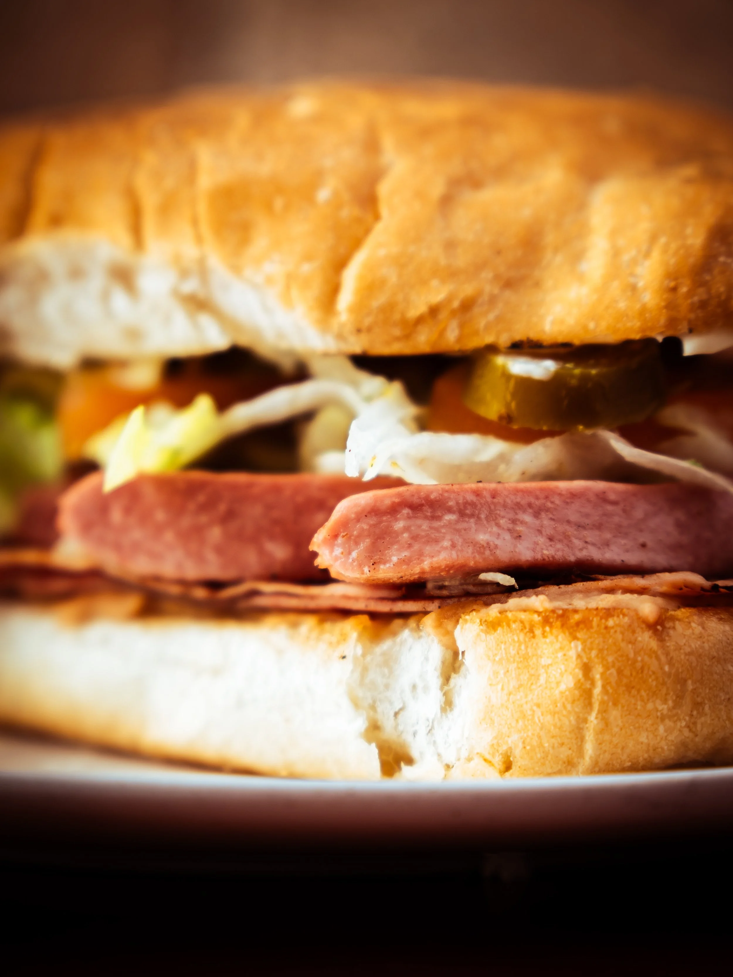 Close-up of a Torta with bread, lettuce, tomato, cucumber slices, deli meats, and mayonnaise inside a toasted sandwich bun.