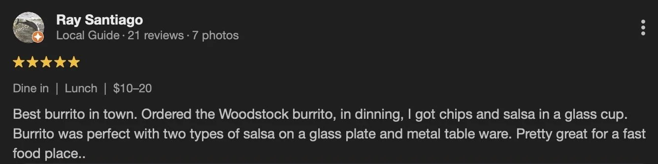 Yelp review for Ray Santiago, a local guide, rating five stars. The review describes a dining experience where the reviewer ordered a Woodstock burrito, chips, and salsa served in a glass cup. The burrito was served with two types of salsa on a glass plate and metal tableware.