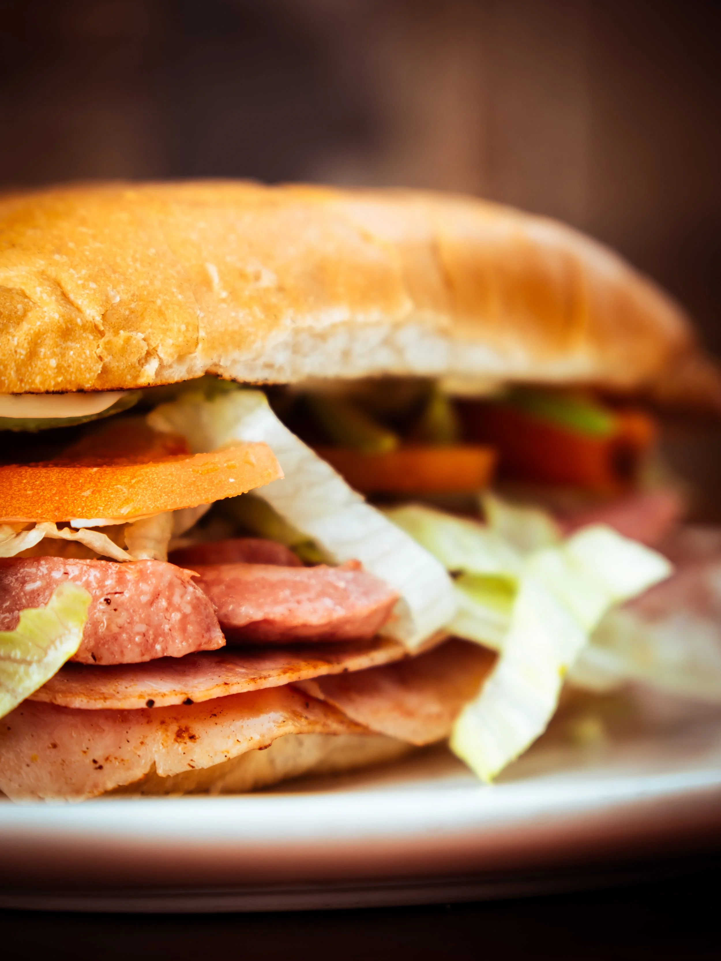 Close-up of a Torta with layers of lettuce, tomato, various deli meats, and a toasted bun.