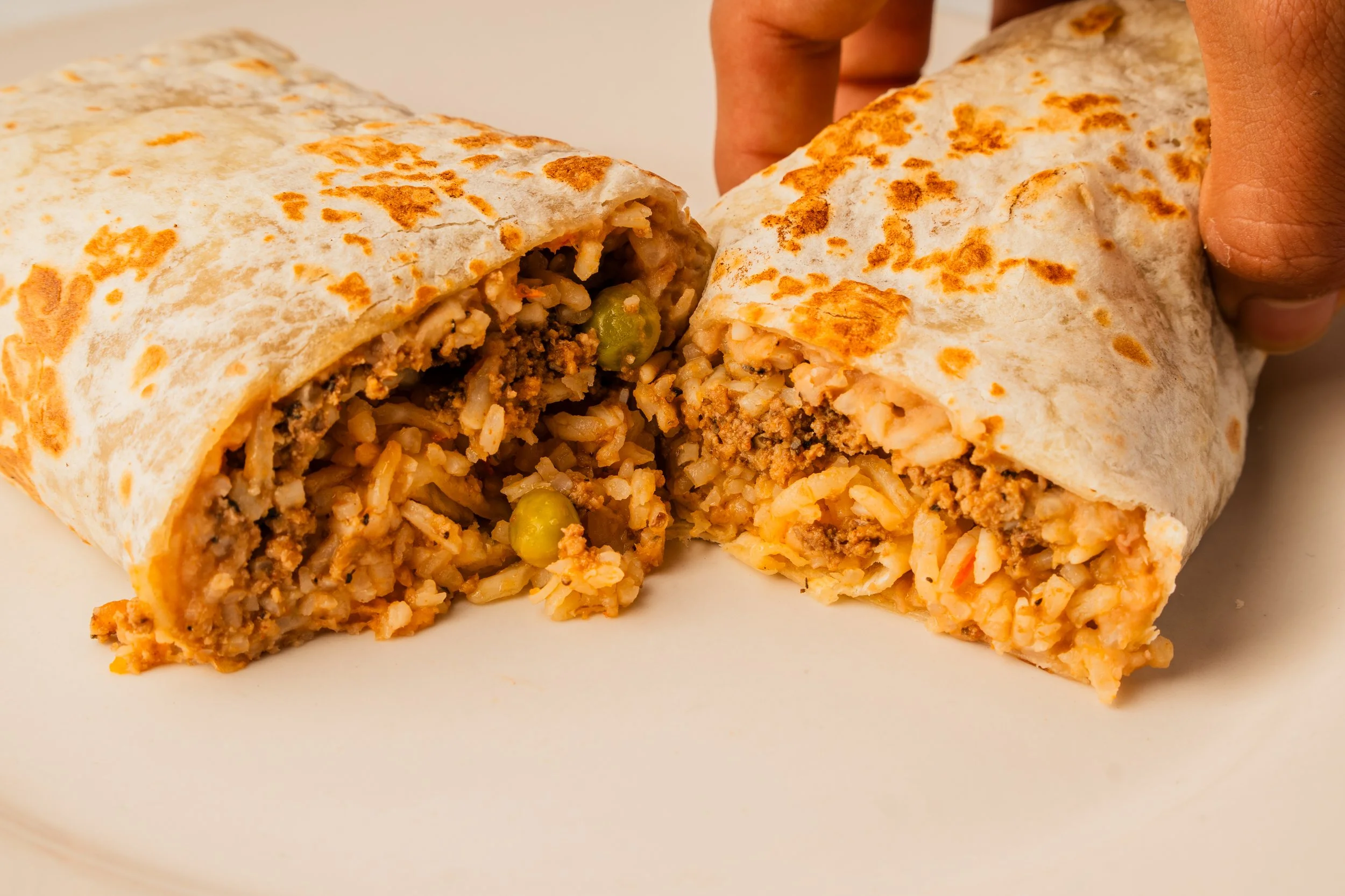 Close-up of a burrito being cut in half, showing seasoned rice, ground meat, beans, and cheese inside a flour tortilla.