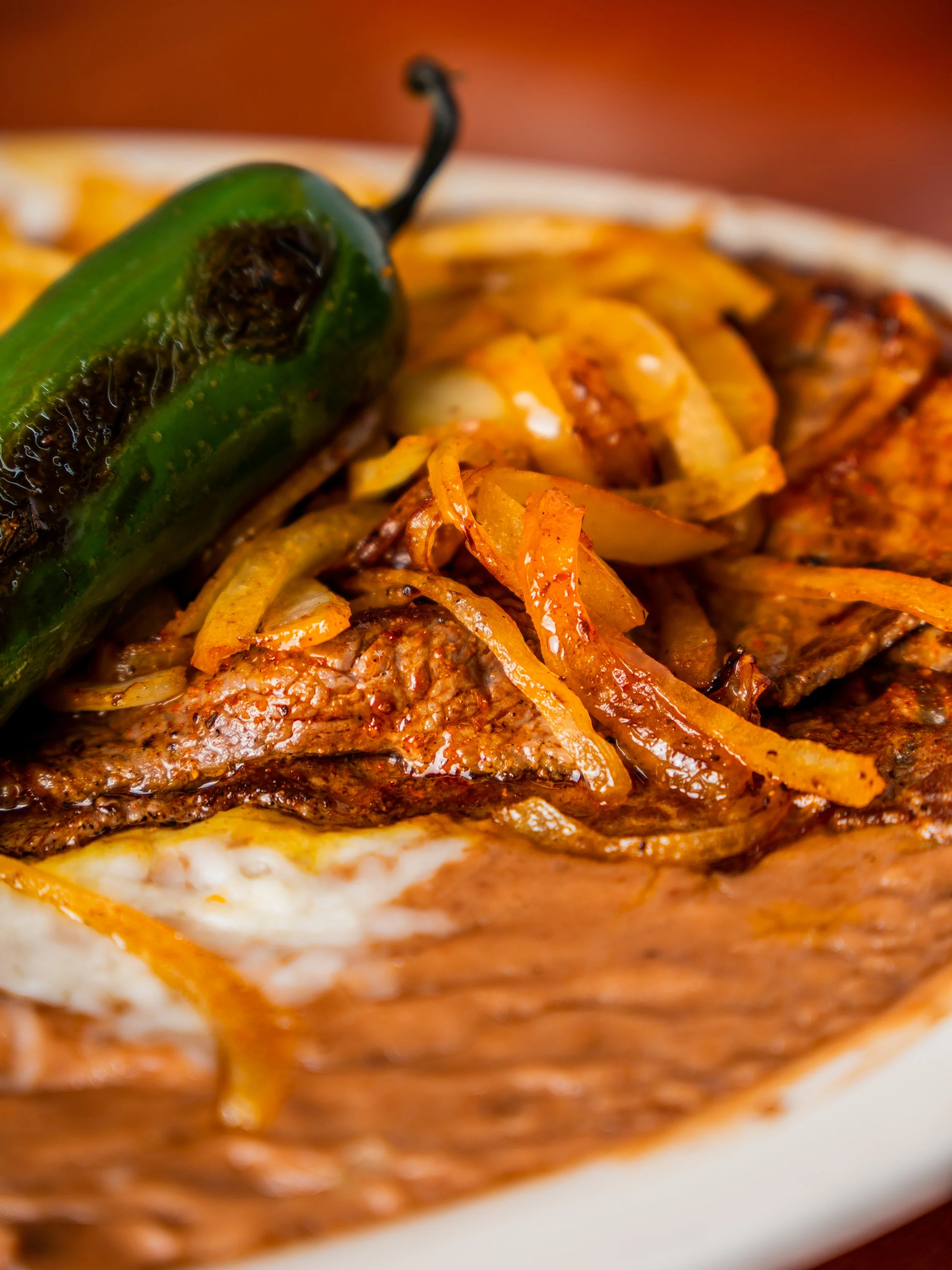 Close-up of a beef steak topped with grilled onions and a roasted jalapeño pepper.