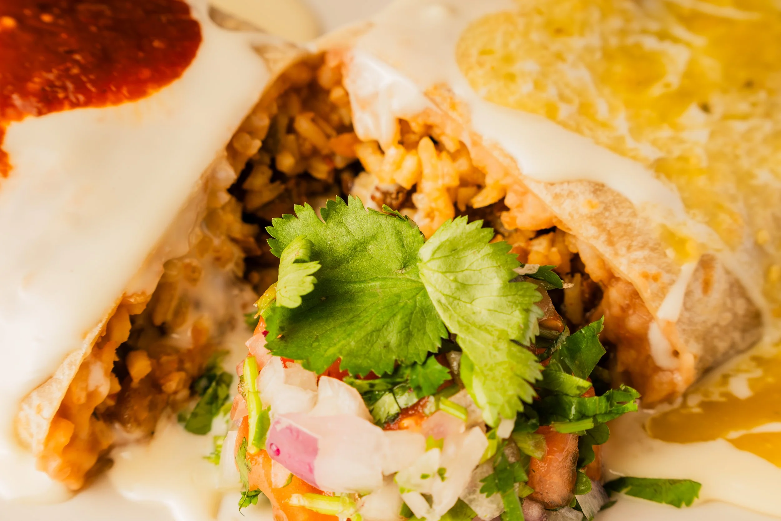 Close-up of a Mexican burrito, filled with rice, meat, fresh cilantro, and shredded vegetables, topped with melted cheese and a garnish of cilantro leaves.