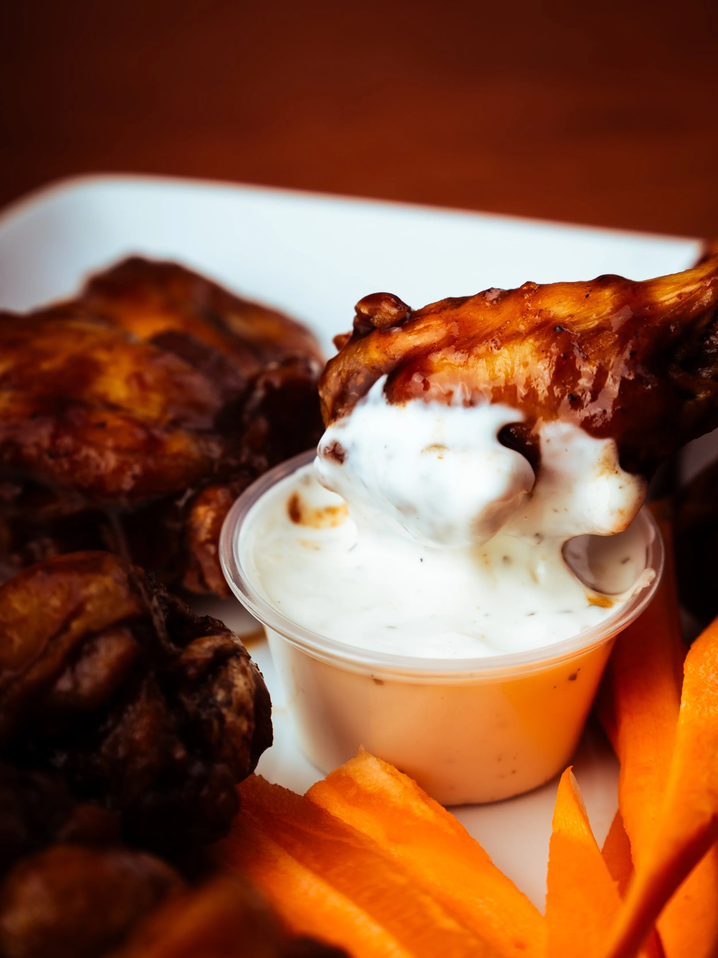 Close-up of buffalo chicken wings with blue cheese dipping sauce, surrounded by carrots.