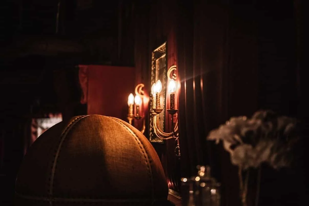 Candlelit brass sconces, red velvet drapes, and a tufted leather chair inside Needle & Thread, a hidden speakeasy in Seattle.