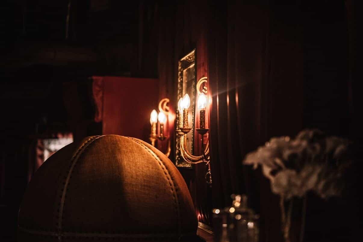 Candlelit brass sconces and red velvet drapes inside Needle & Thread, the speakeasy above Tavern Law in Seattle.