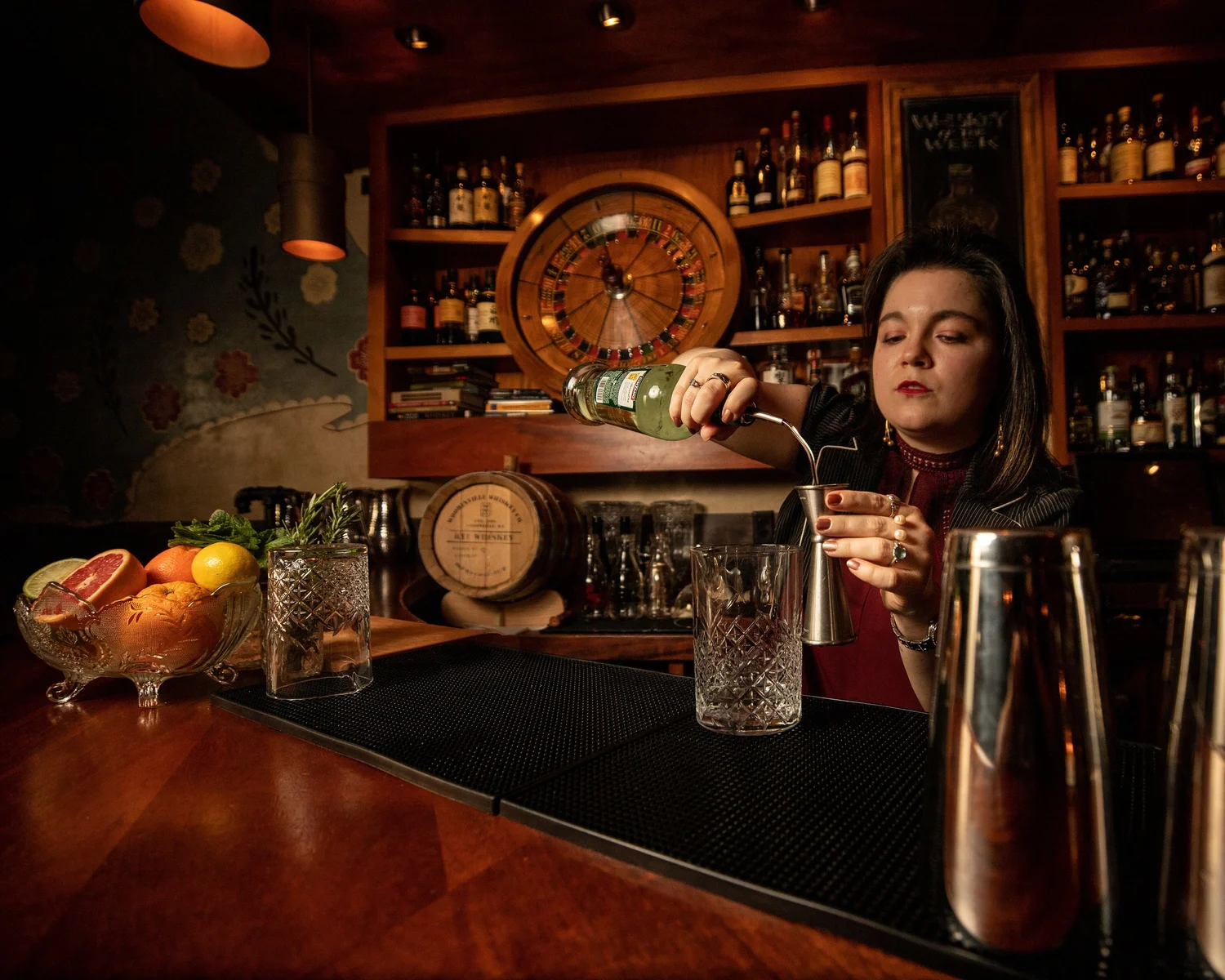 A Tavern Law bartender pouring a measured cocktail in front of the backbar.