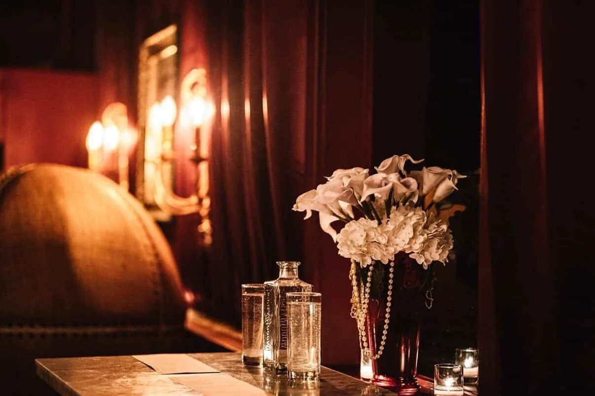 A private event setting at Tavern Law in Seattle, with white flowers and pearls, candlelight, and red velvet drapes.