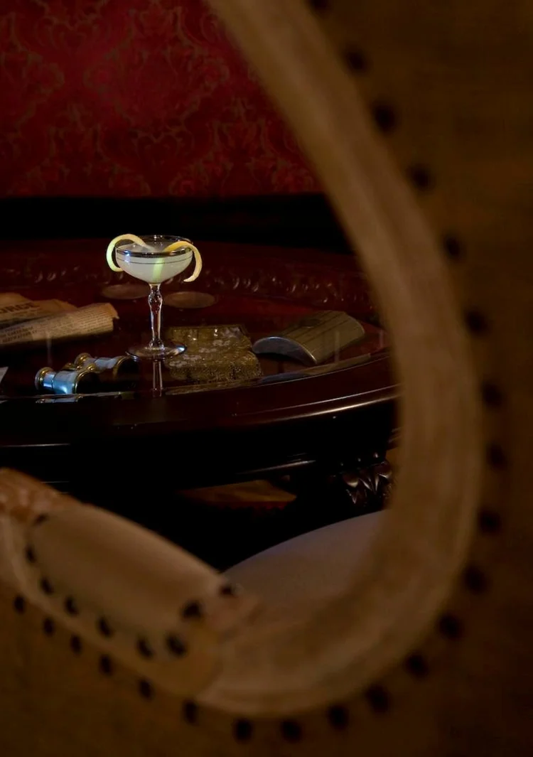 A coupe cocktail on a candlelit table, framed by a chair back inside Needle & Thread.