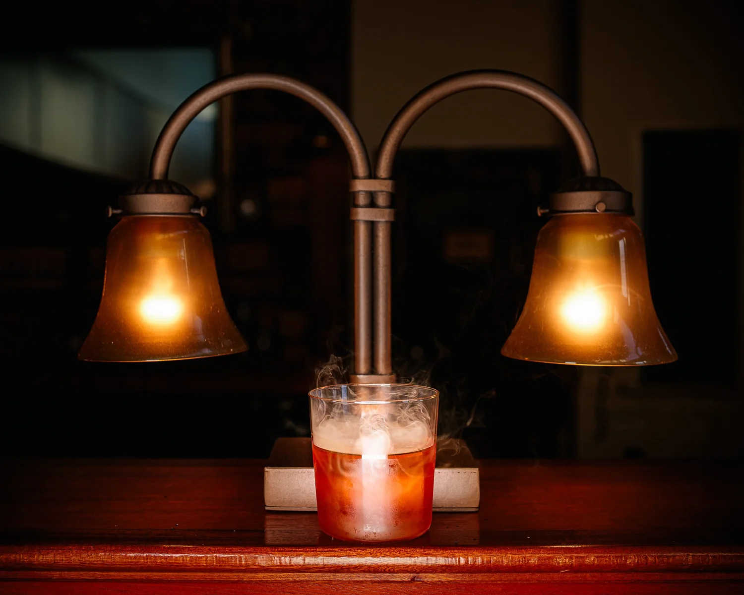 A smoking cocktail beneath a brass double lamp on the bar at Tavern Law, a craft cocktail bar on Capitol Hill.