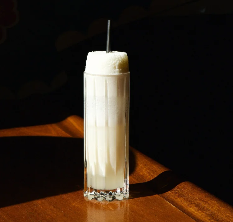 A tall foam-topped fizz cocktail with a metal straw at the Tavern Law bar.