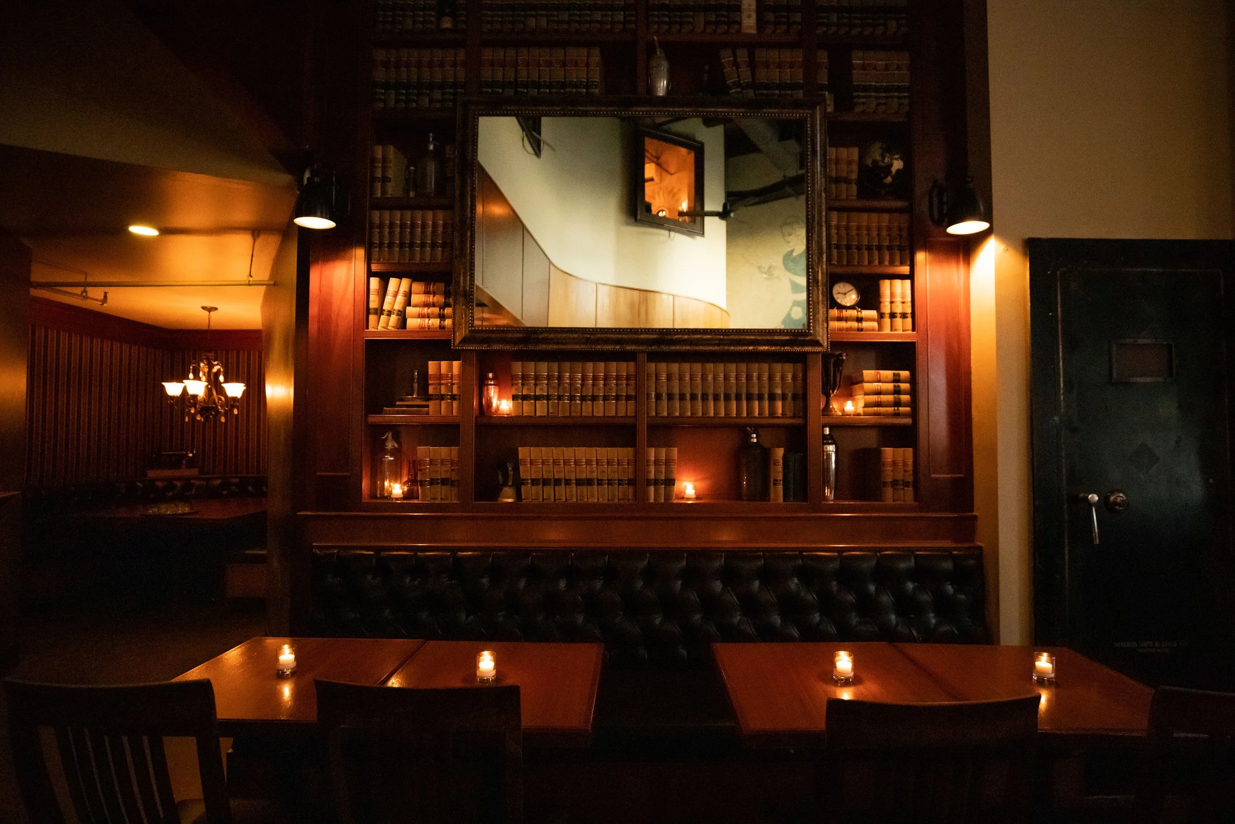 The candlelit dining room at Tavern Law on Capitol Hill, with law-book shelves, leather banquettes and the vault door to the speakeasy