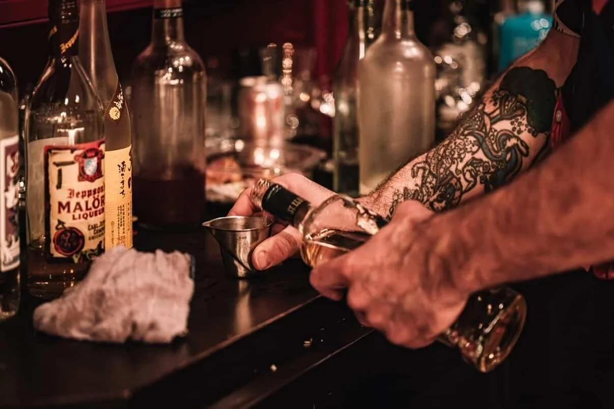 A Needle & Thread bartender measuring a pour for a bespoke cocktail built to a guest's taste, upstairs at the Seattle speakeasy.
