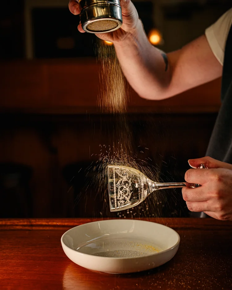 A bartender dusting a sugar garnish over a crystal coupe at Tavern Law.