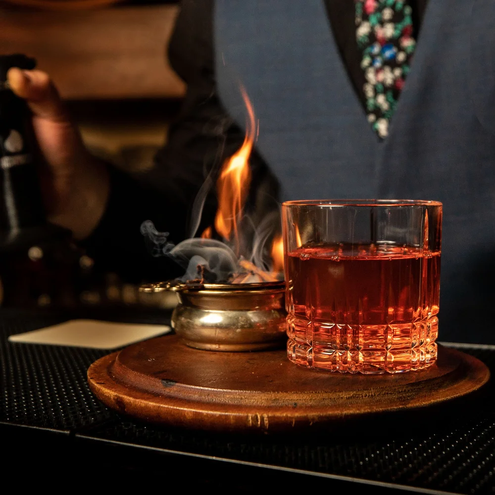 Smoked cocktail served over ice beside a flaming brass vessel at Tavern Law in Seattle