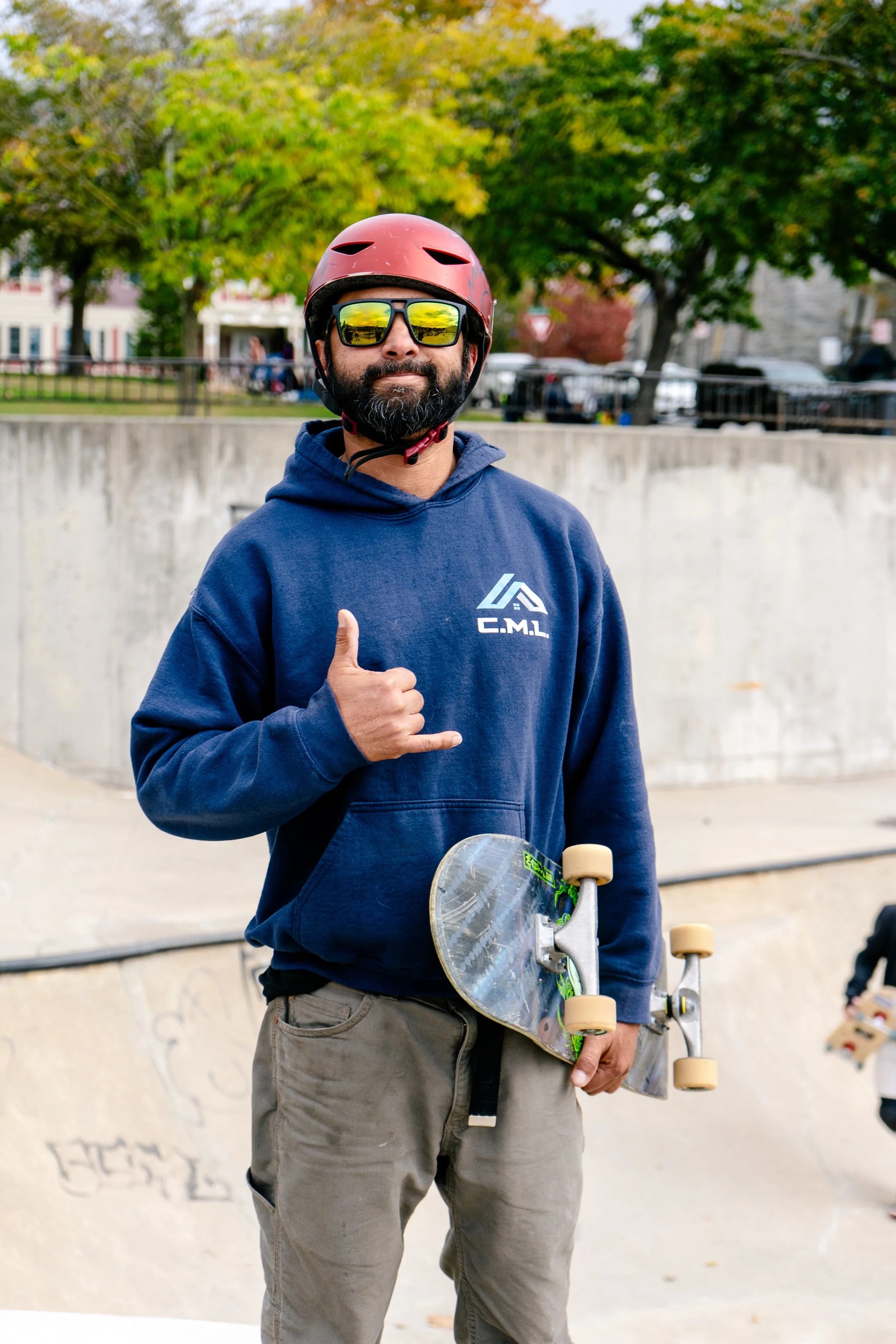 A man with sunglasses and a skateboard gives a thumbs-up at a skate park.